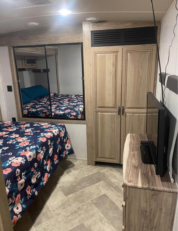 RV rental bedroom interior: floral bed, mirrored bunk reflection, wooden closet, and TV stand. Cozy travel accommodations.. Palomino Solaire 2021