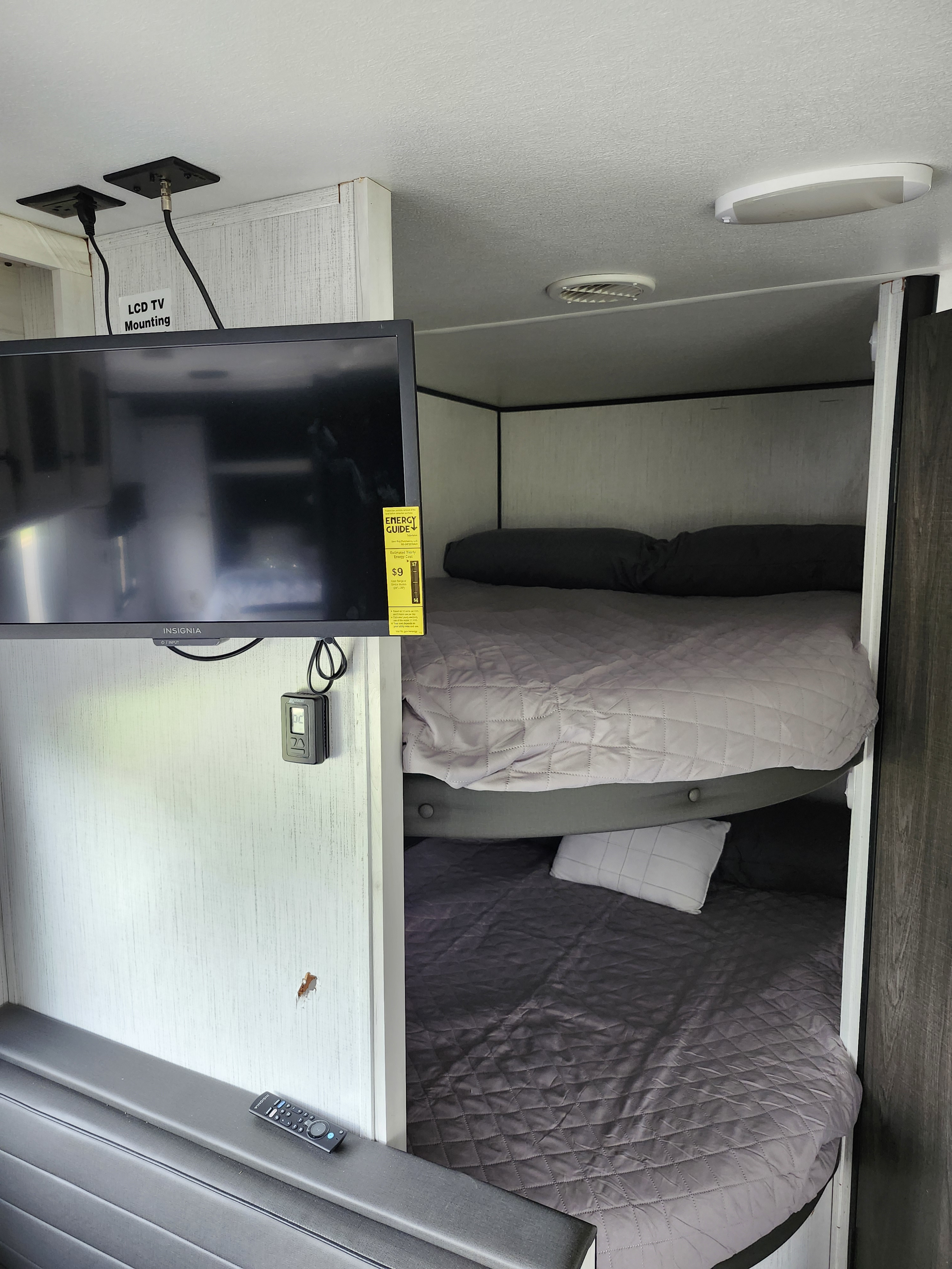 Interior of an RV rental showing stacked bunk beds on the right and a wall-mounted TV with a remote on the left.. Heartland RVs Trail Runner 2022