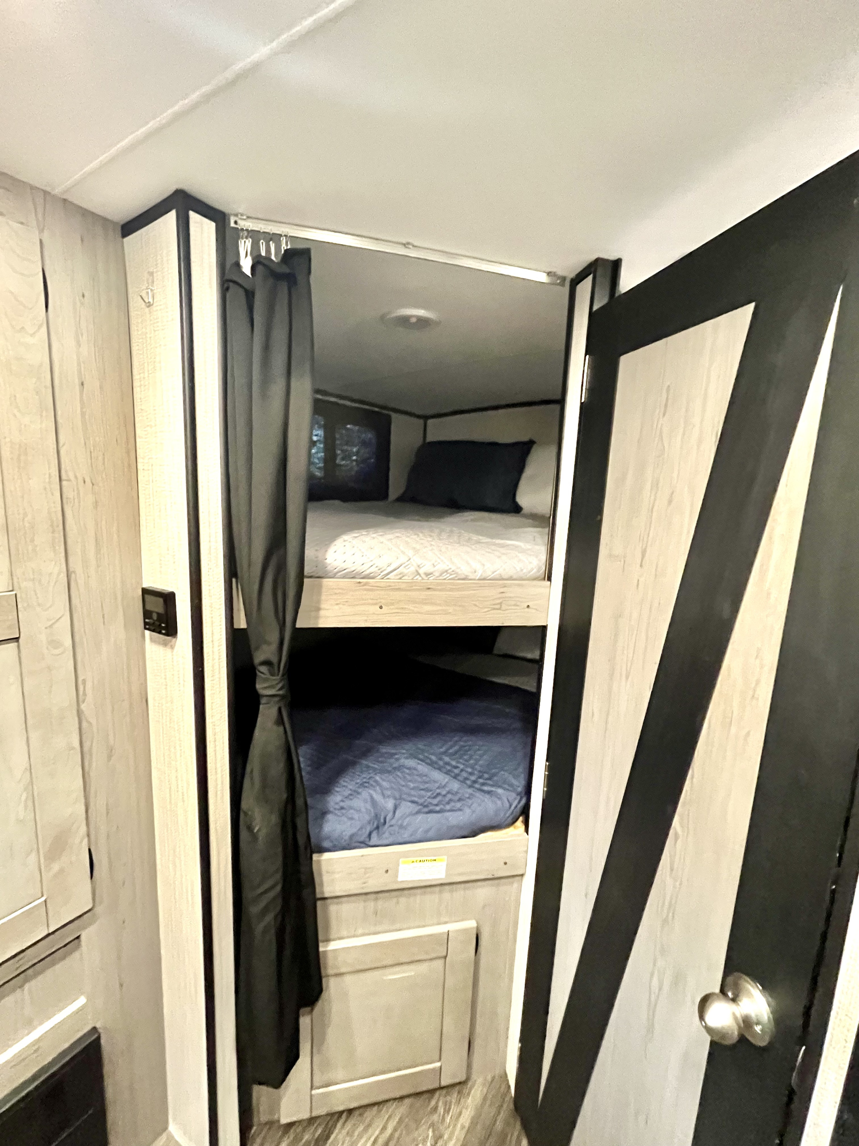 An RV rental's compact sleeping area featuring two bunk beds with blue and white bedding, a privacy curtain, and modern wood-look finishes.. Heartland M-3385 2021