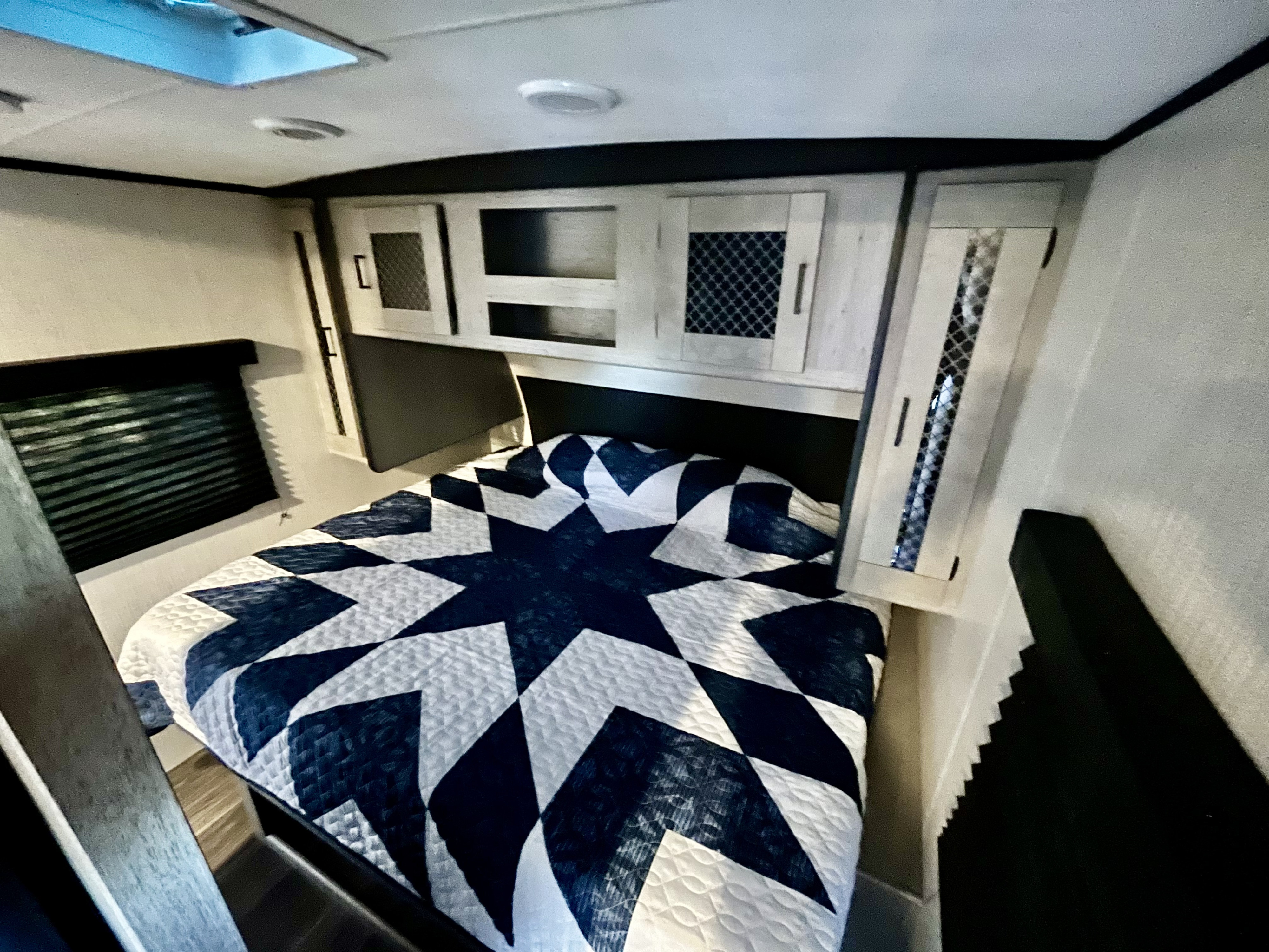 Interior of an RV rental bedroom featuring a bed with a blue and white star quilt, overhead cabinets, and a ceiling skylight.. Heartland M-3385 2021