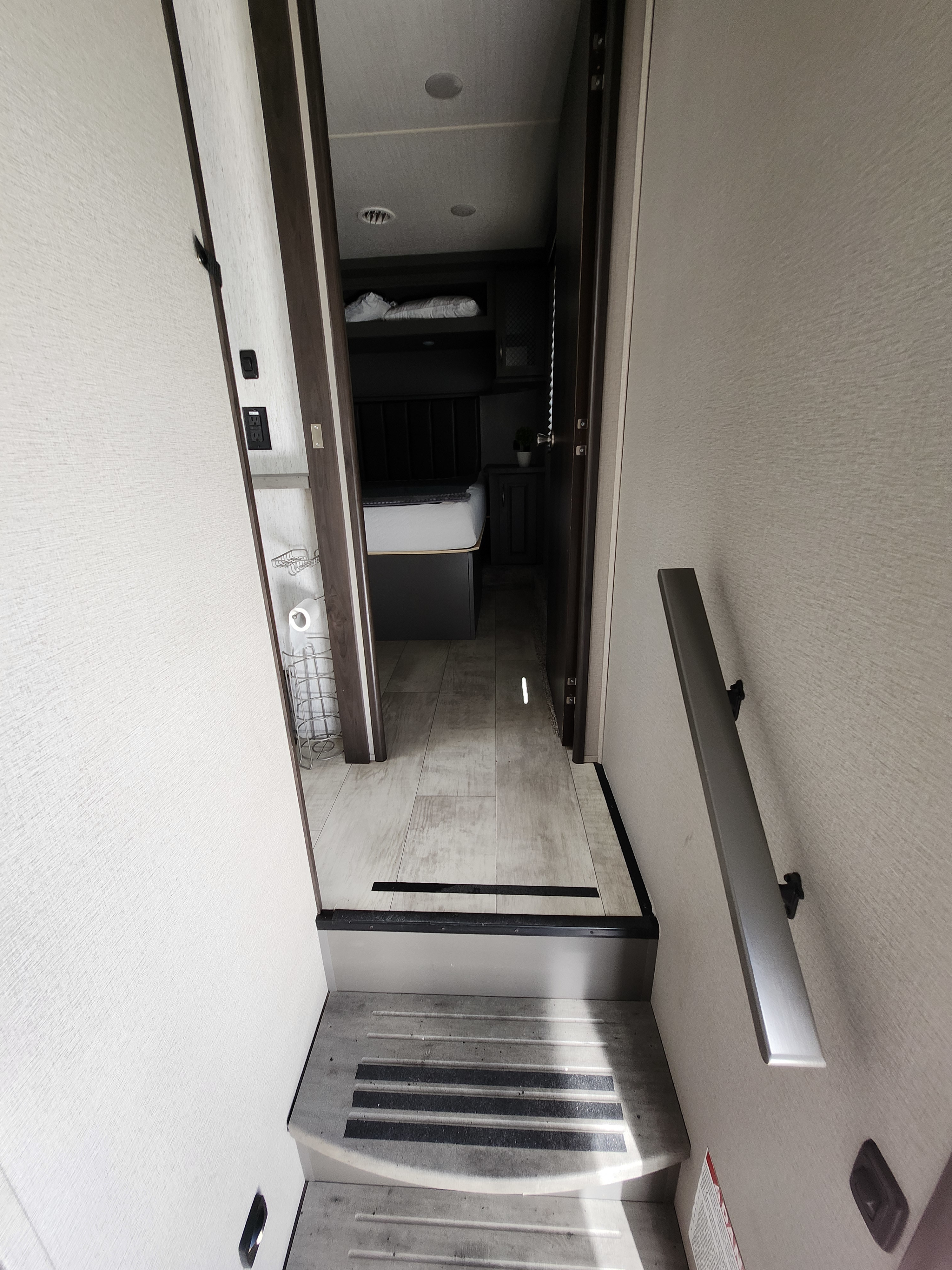 RV rental interior: Steps descend into a hallway. An open doorway reveals a compact bedroom area. A handrail aids descent.. Grand Design Momentum 2021