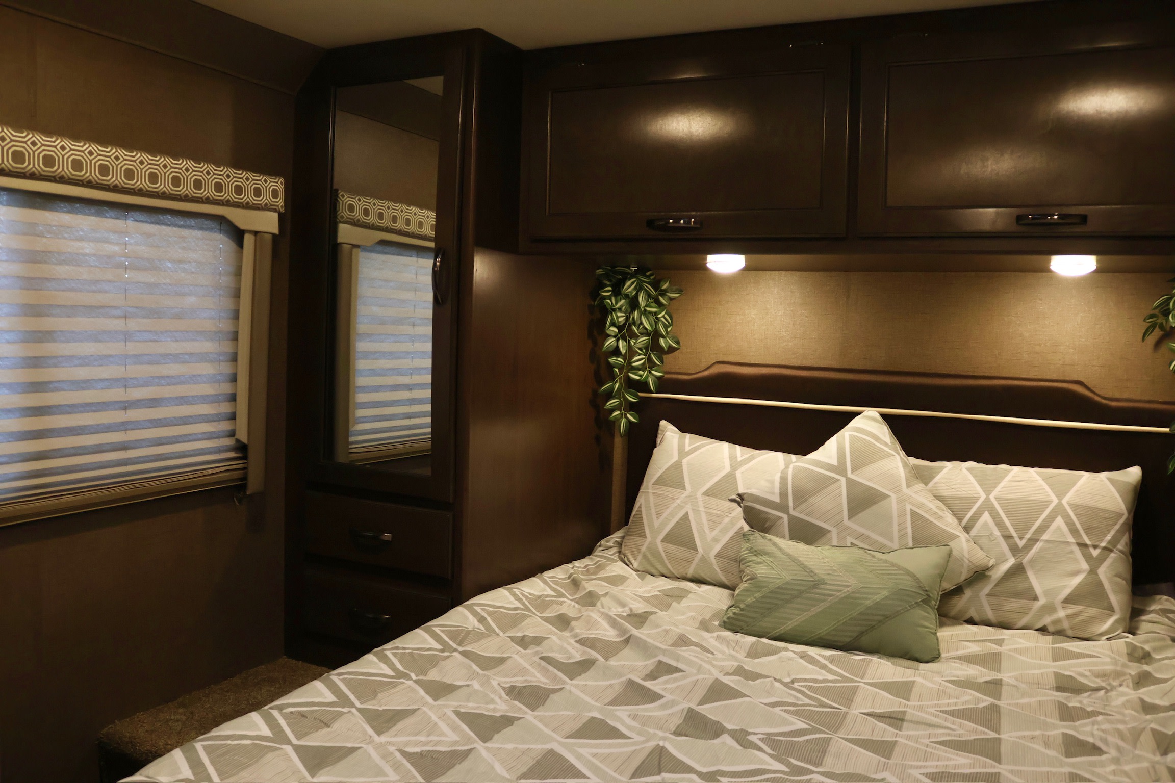 Cozy RV rental bedroom with dark wood cabinets, striped window, and bed with geometric patterned bedding.. Thor Four Winds 2019