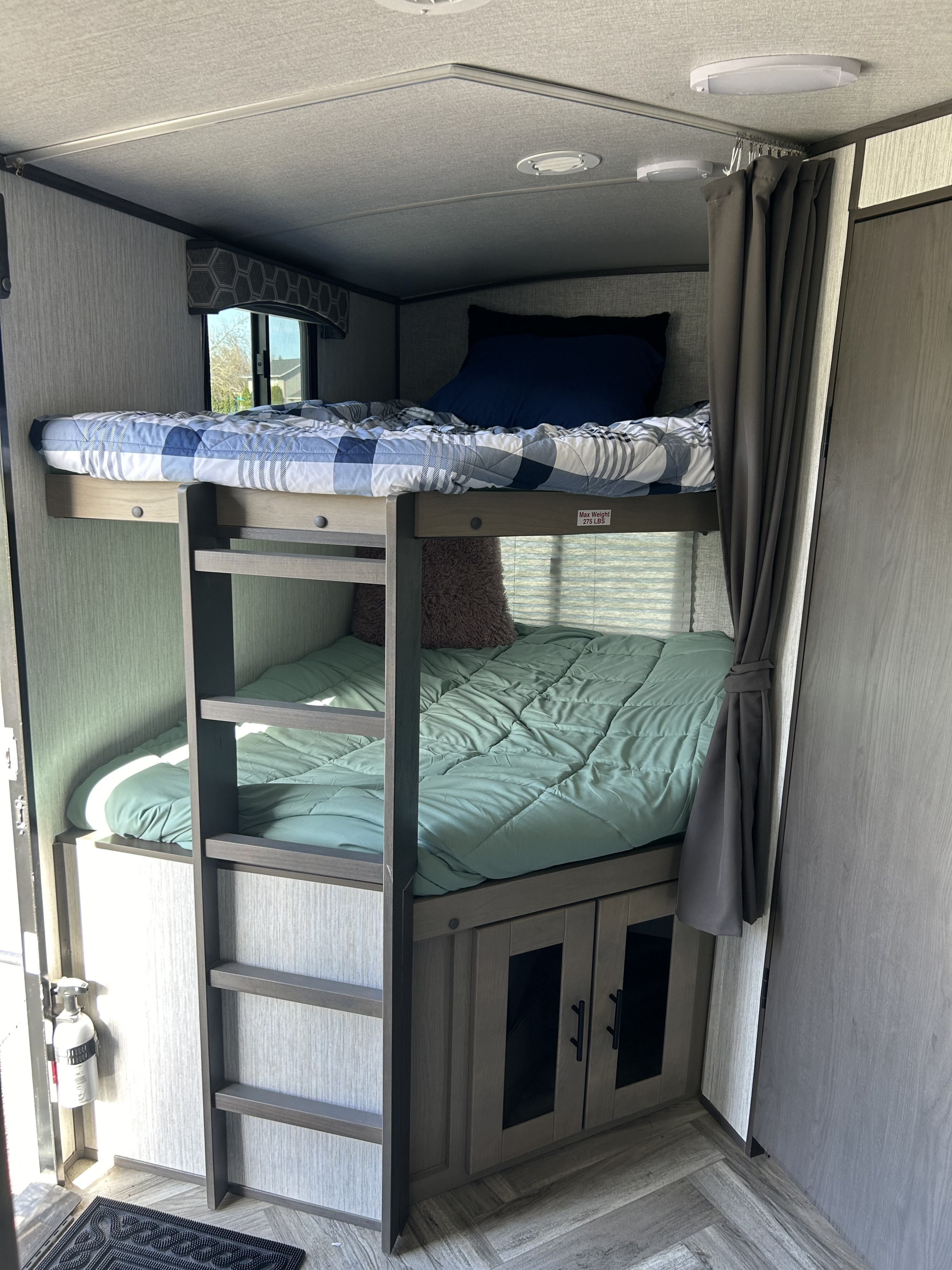 Cozy RV rental interior with bunk beds. Upper bed has blue plaid, lower has green, with ladder & cabinet storage. Ideal compact sleeping.. Shadow Trailers Shadow Cruiser 2020