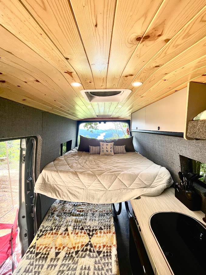 Explore this spacious RV rental interior: wood ceiling, elevated bed, lower sleeping, compact kitchen, & scenic lake view.. Ford Transit 350 High roof 2020