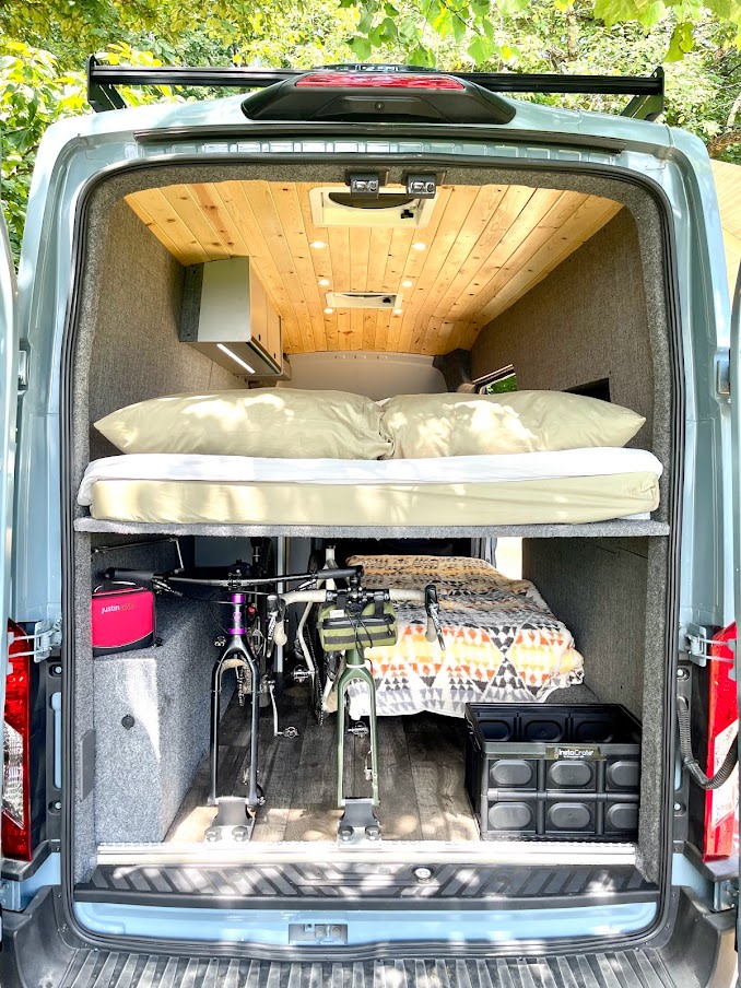 This RV rental's rear interior features an upper bed, bikes secured below, and a lower bed with storage crate.. Ford Transit 350 High roof 2020