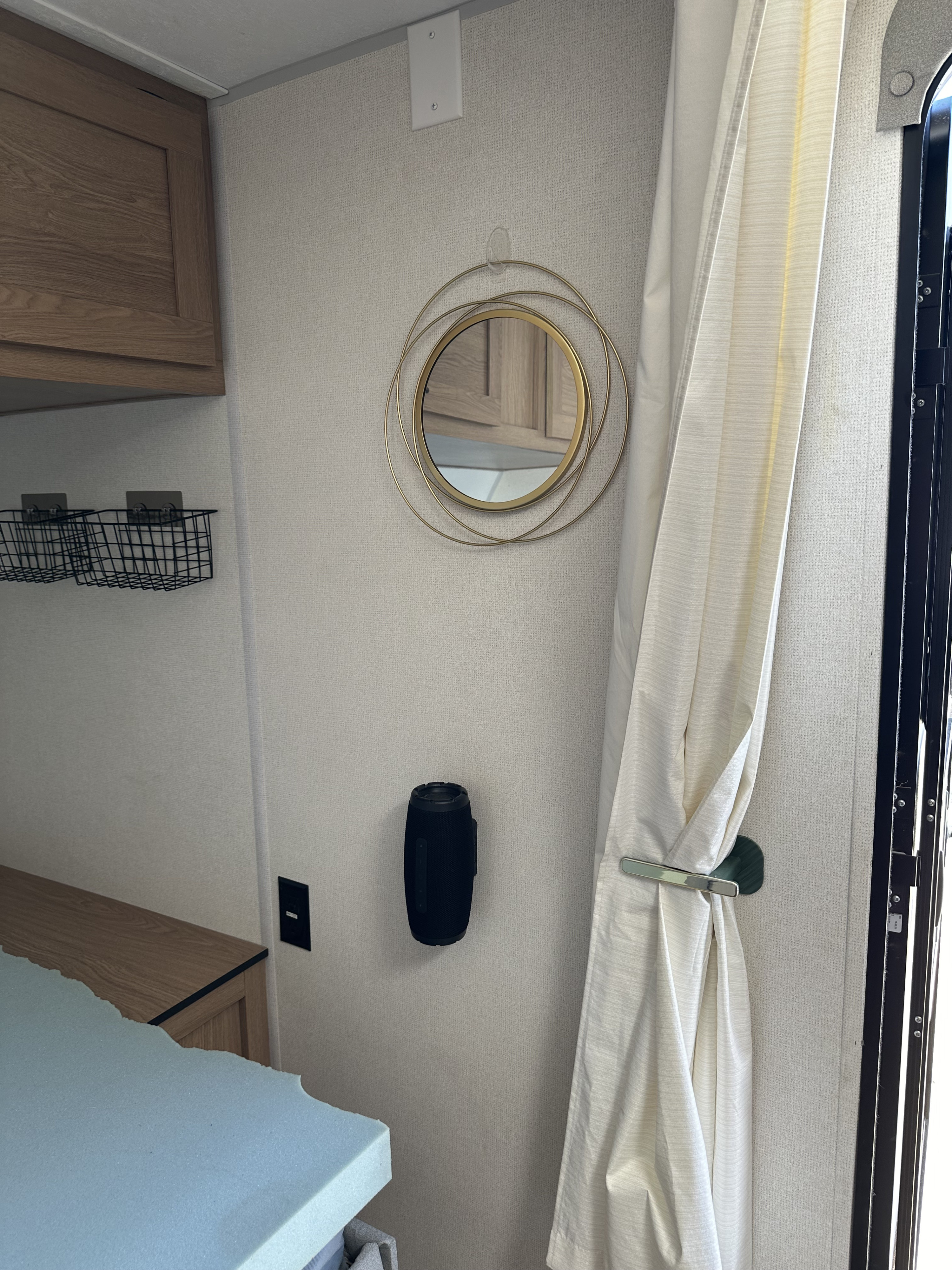RV rental interior: wood cabinets, wire baskets, a mirror, speaker, and tied-back curtain by the door.. Prime Time Avenger - 17BHS 2022