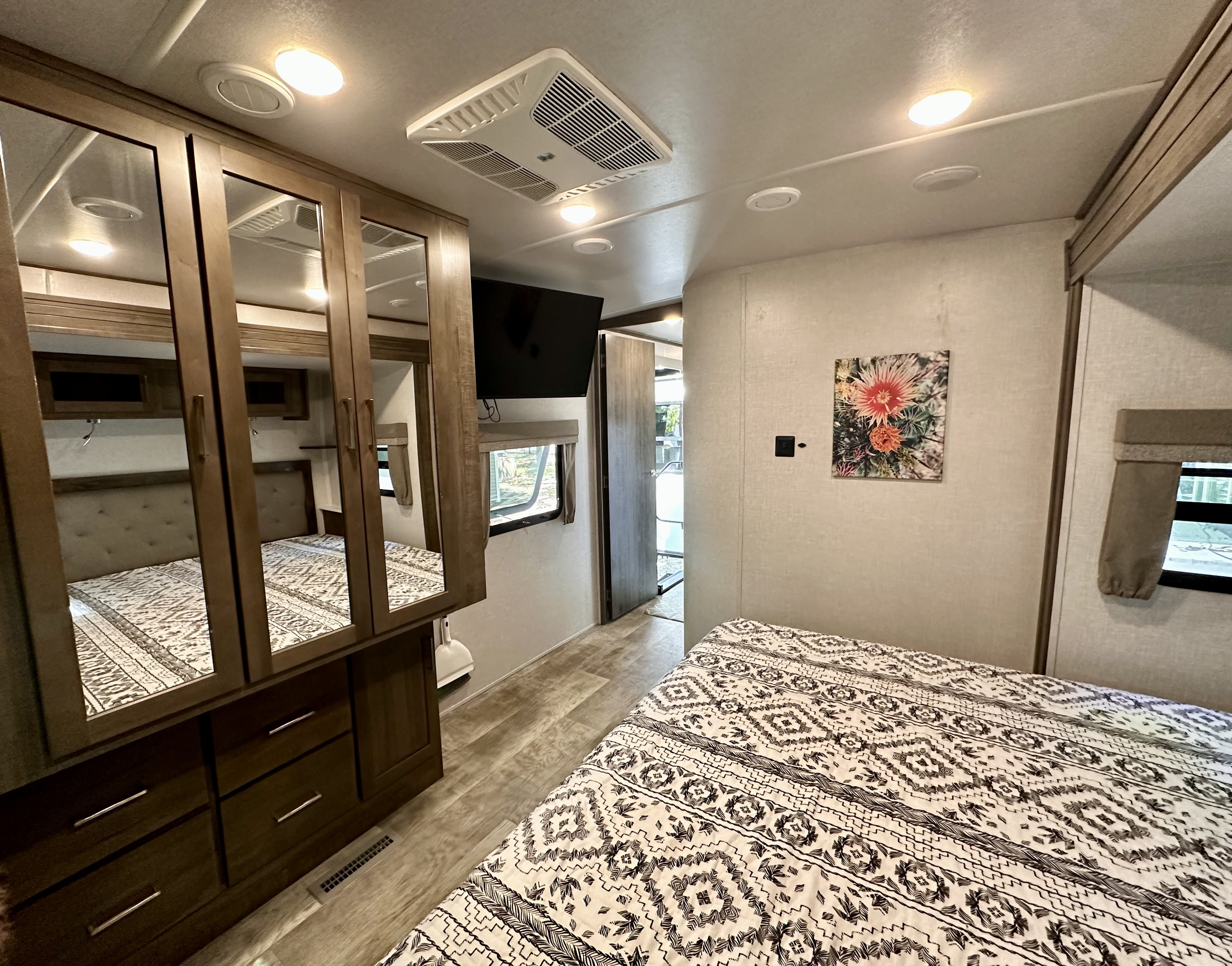 RV rental bedroom: a cozy space with a patterned bedspread, mirrored wardrobe, wall-mounted TV, and overhead AC.. Forest River Flagstaff Classic 2022