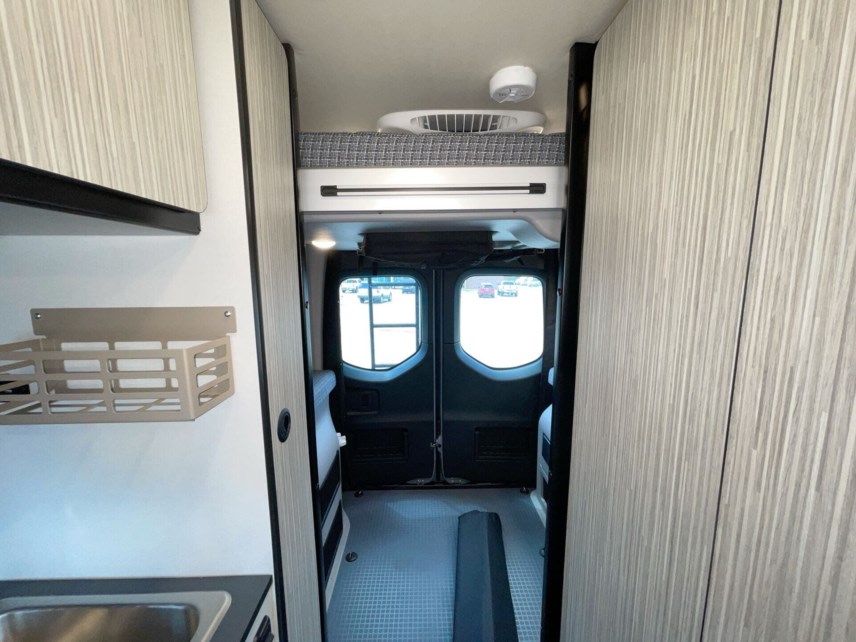 Inside a modern RV rental: a streamlined kitchen with storage, a fan, and a cozy loft sleeping area at the back.. Winnebago Revel 2024