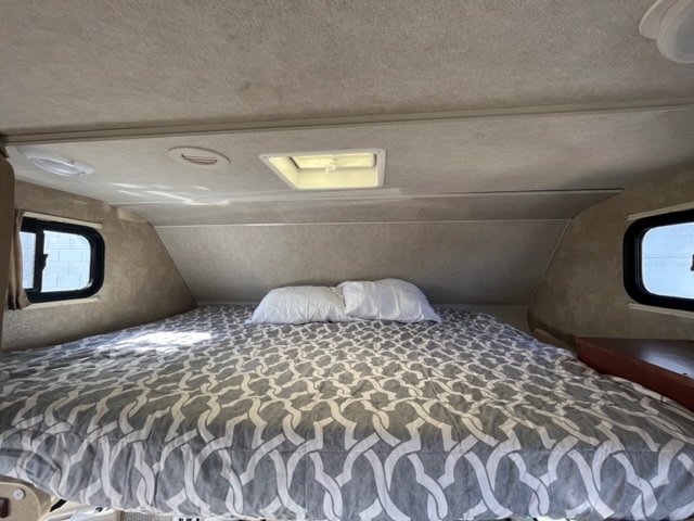 Comfortable RV rental bed with grey patterned comforter, windows, and ceiling vents. Ideal camper sleeping space.. Winnebago Chalet 2014