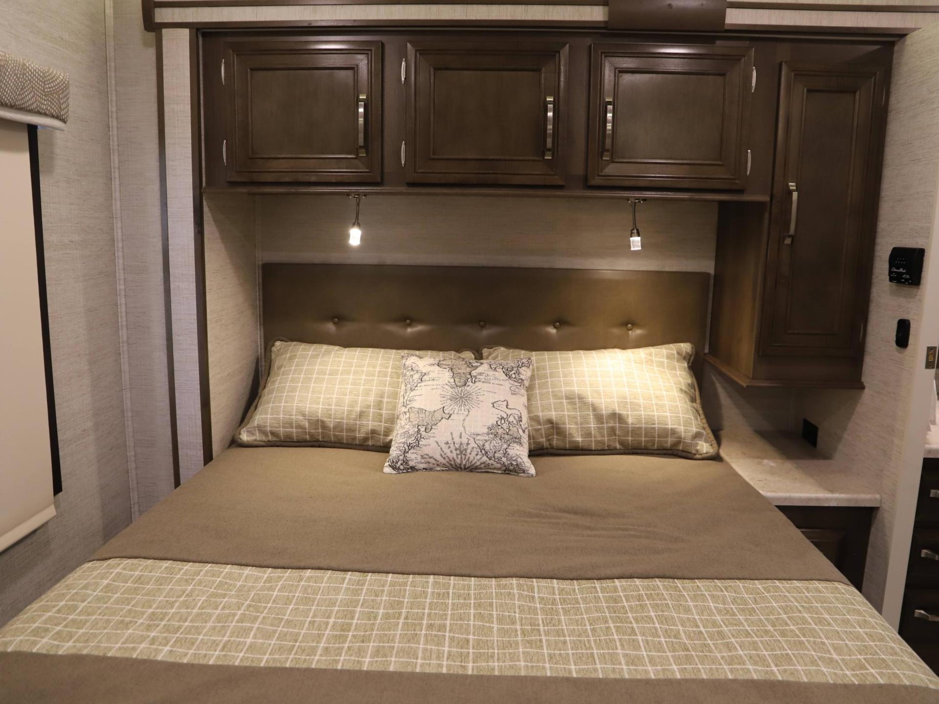 Cozy RV rental bedroom with patterned bedding, padded headboard, and storage cabinets above, ready for a comfortable stay.. Entegra Coach Esteem 2021