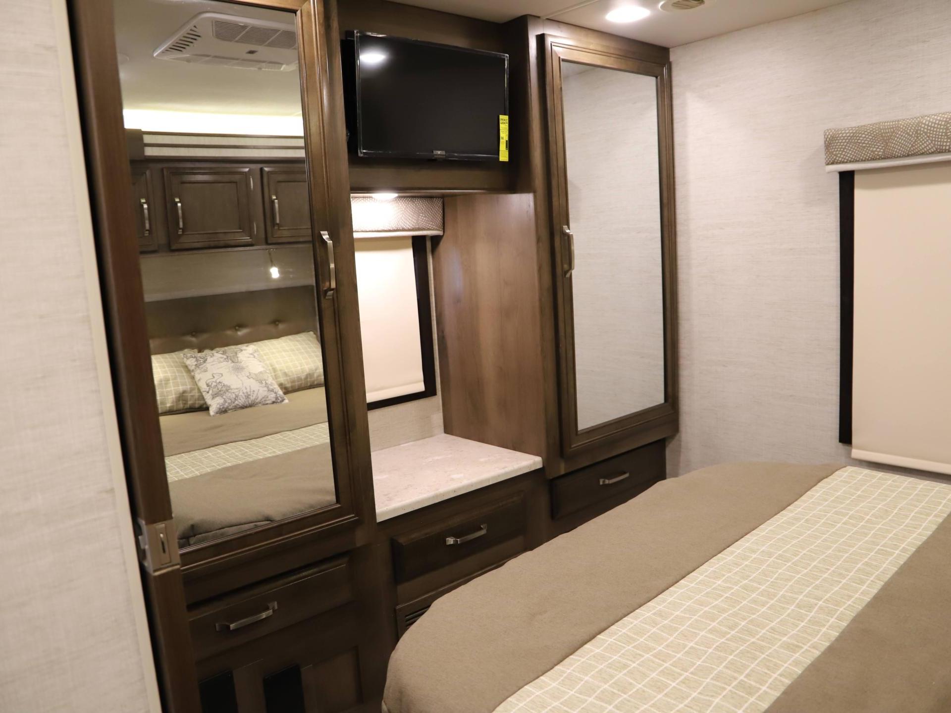Inside an RV rental: a cozy bedroom with a neutral-toned bed, mirrored closets, and a built-in TV for comfort.. Entegra Coach Esteem 2021