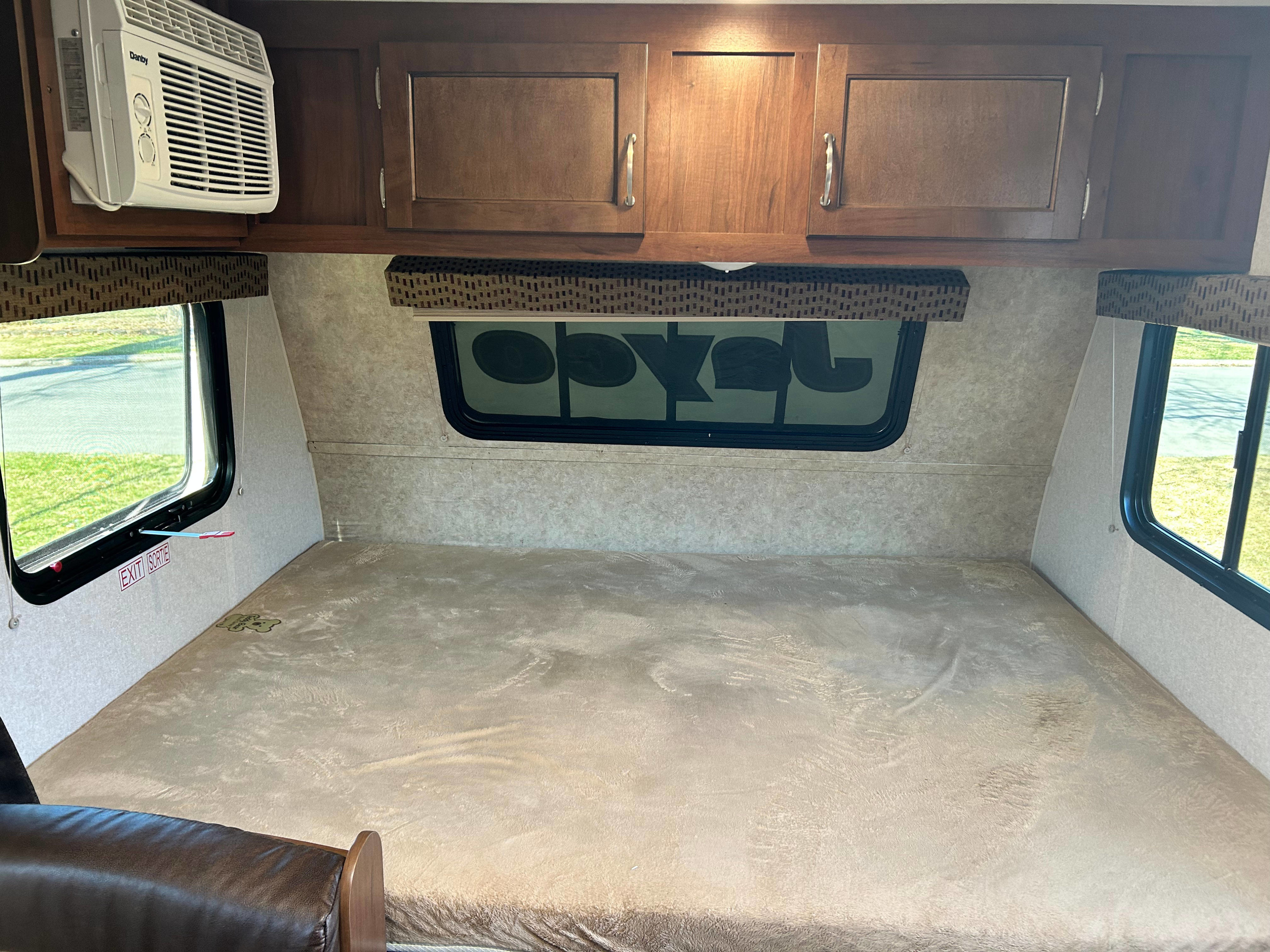 RV rental interior: A comfortable bed with windows, overhead cabinets, and a prominent AC unit.. Jayco Jay Flight SLX 2017