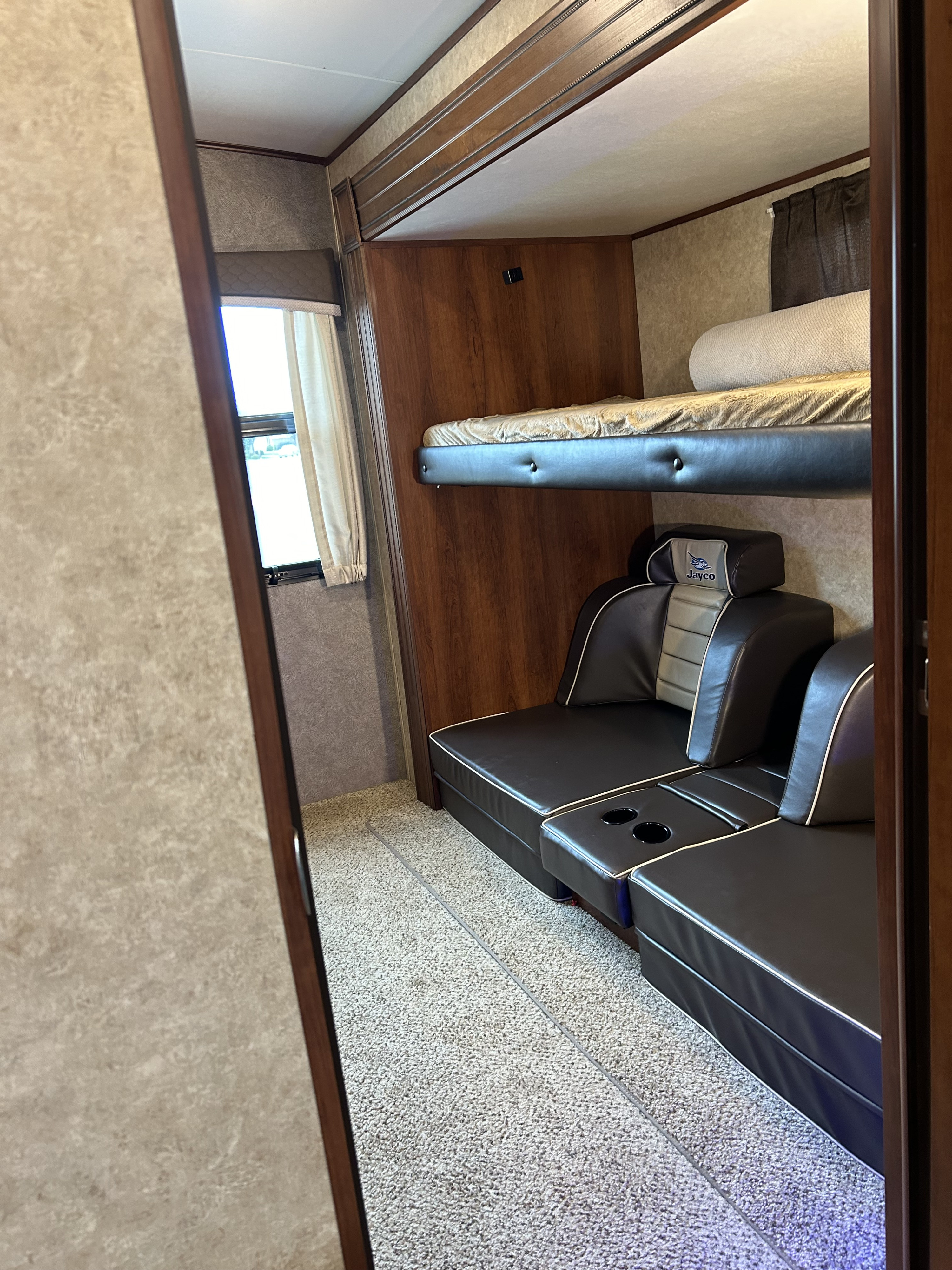 Inside an RV rental: Jayco bunk beds over convertible lounge seating by a window, ideal for travel.. Jayco Eagle HT 2018