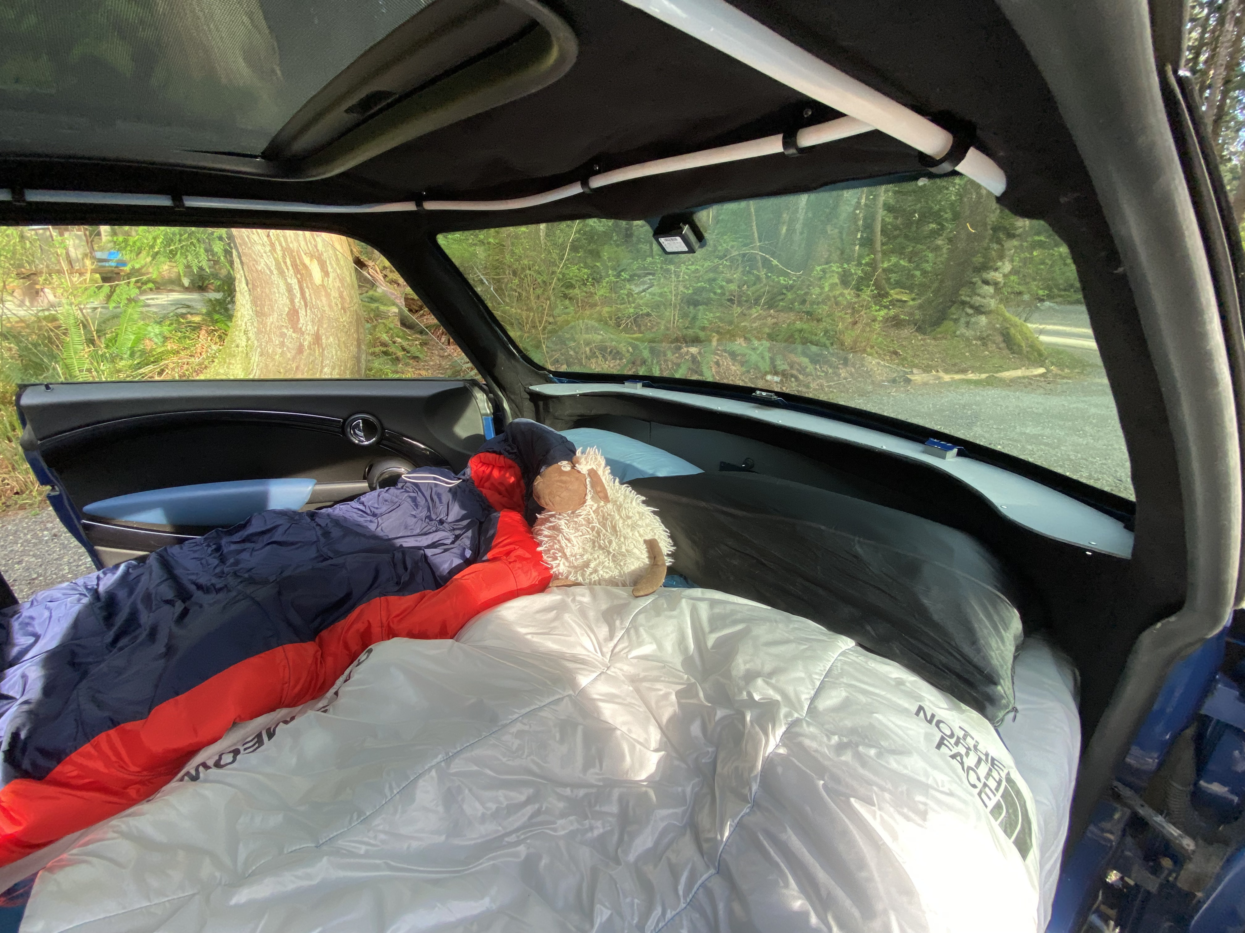 Cozy car camping setup inside a Mini Cooper with sleeping bag and pillows. A compact alternative to a traditional RV rental.. MINI Cooper 2007