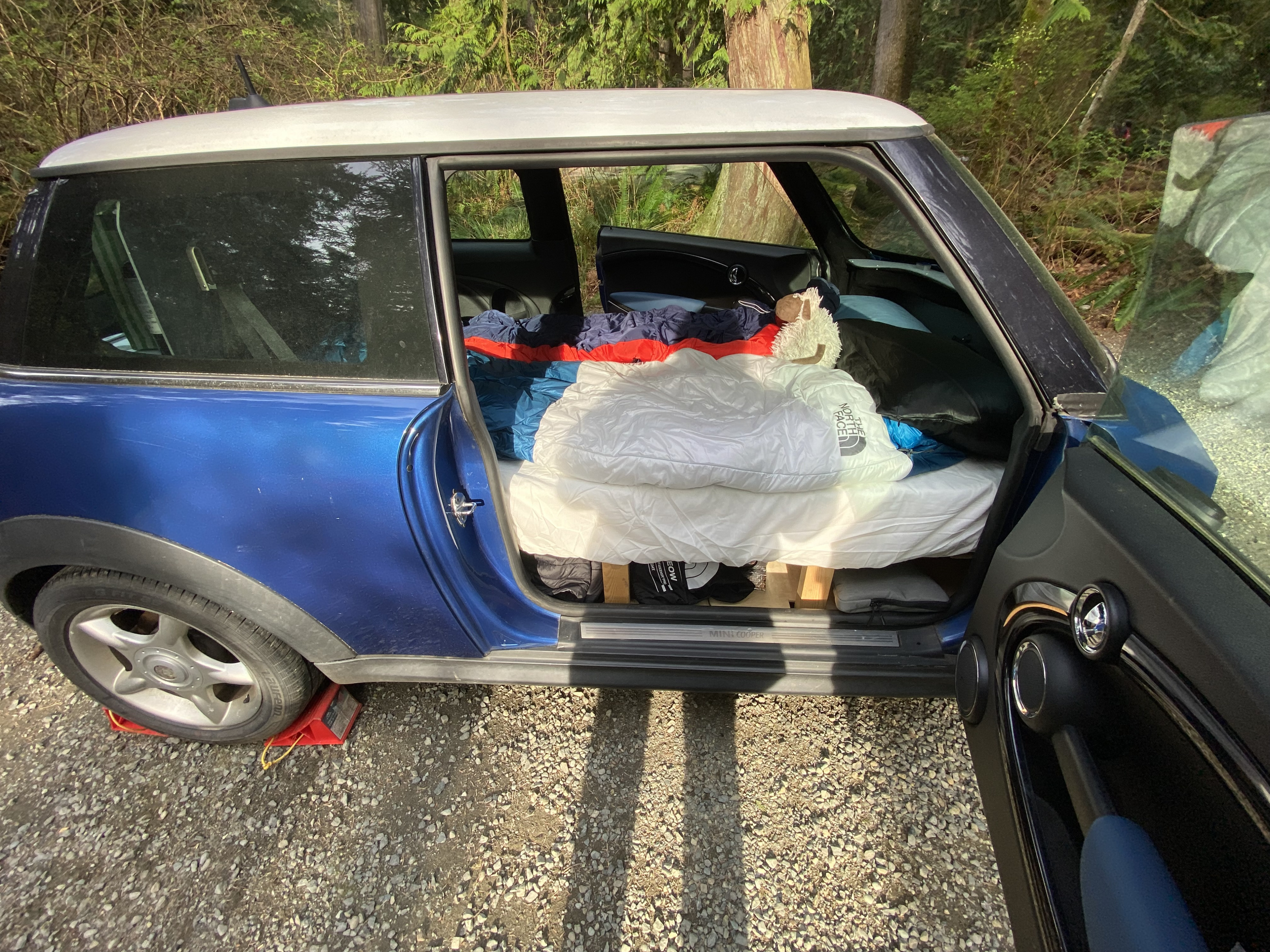 Blue Mini Cooper DIY car camping setup with bed platform & sleeping bag, a compact RV rental alternative.. MINI Cooper 2007