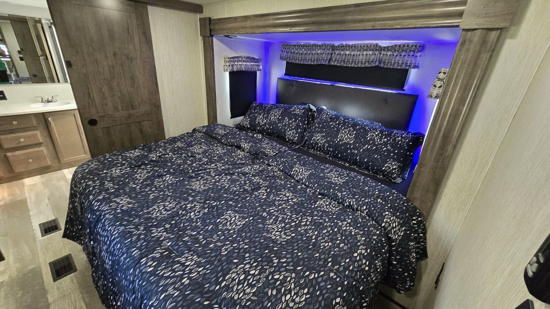 Spacious RV rental bedroom featuring a patterned bed, blue LED lighting, and adjacent bathroom access. Comfort on the go.. Forest River Sandpiper 2021