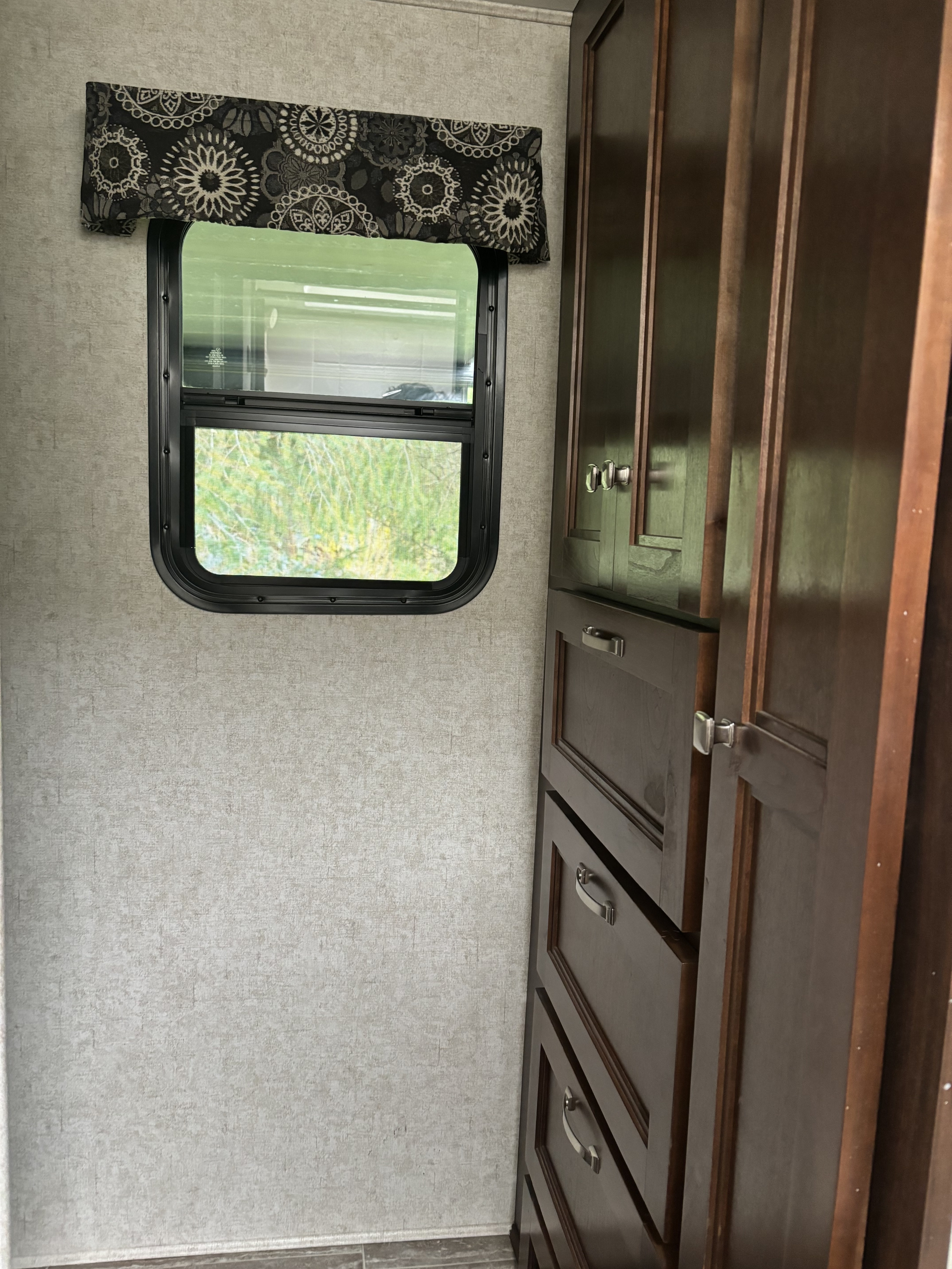 View inside an RV rental: Features a window with a patterned valance and dark wood cabinets with silver hardware.. Forest River Sunseeker 2018