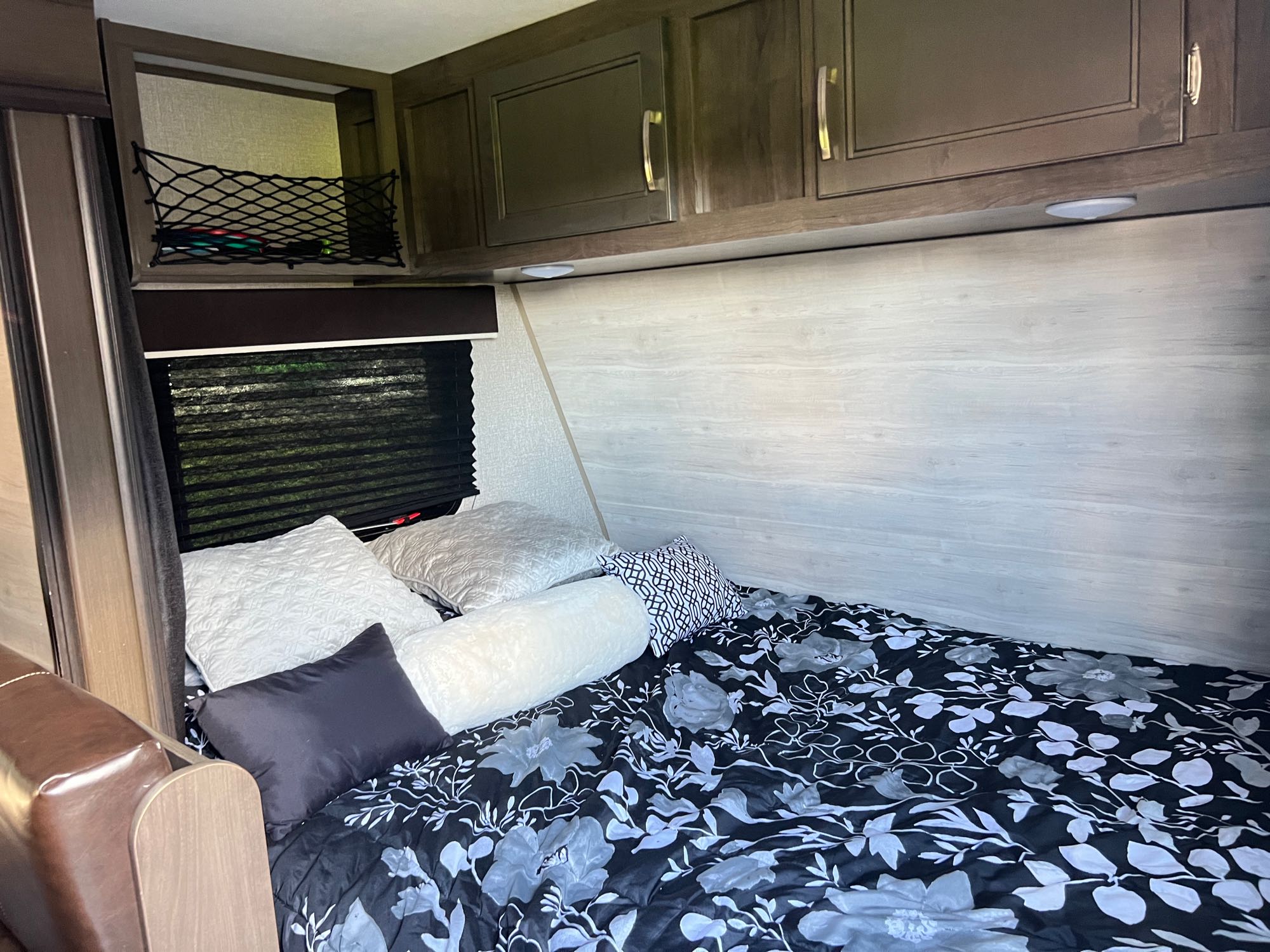 Cozy RV rental bedroom with a floral comforter, various pillows, overhead cabinets, and window blinds.. Jayco Jay Flight 2021