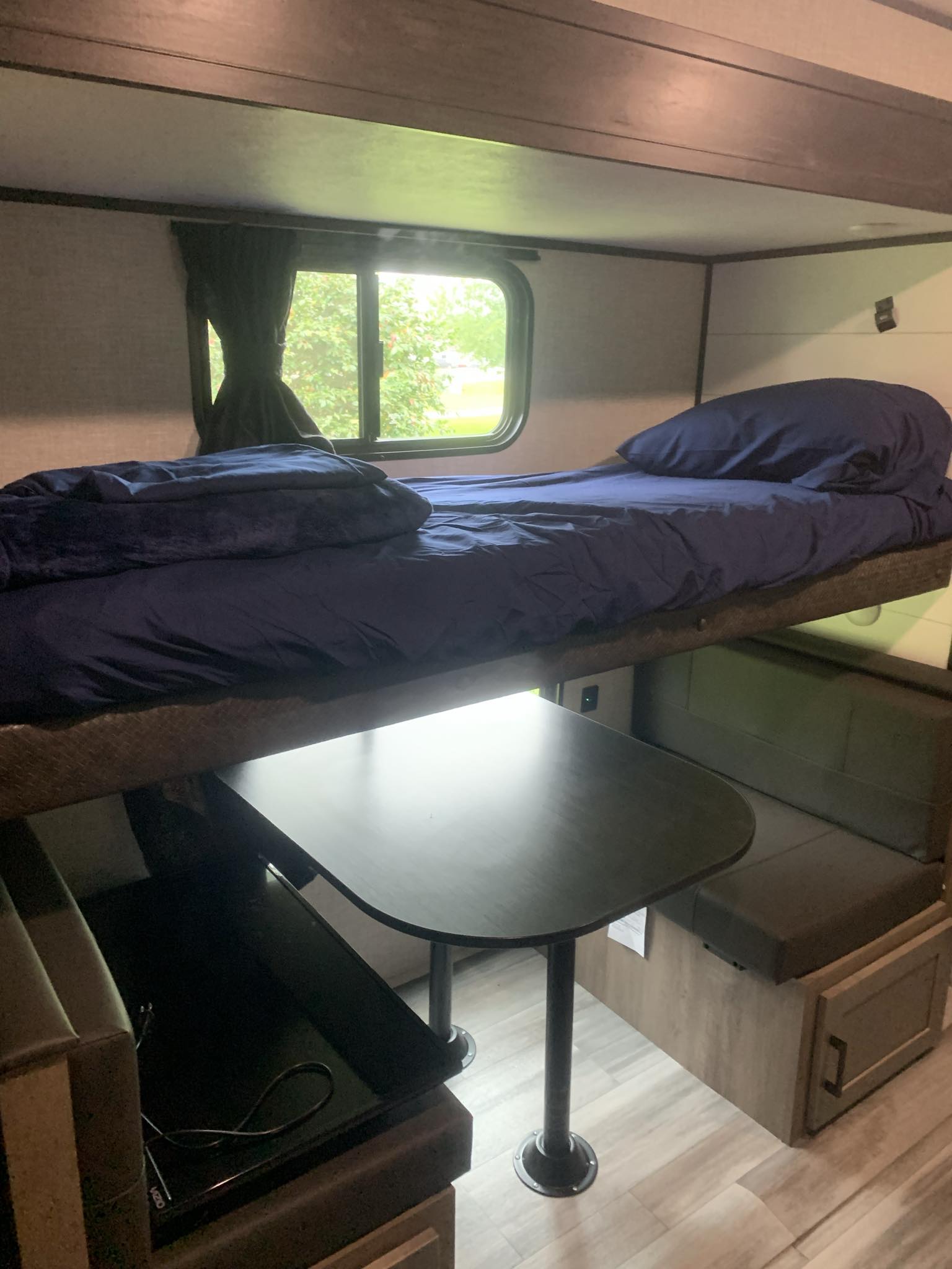 An RV rental interior featuring a comfy navy bunk bed above a dining table with bench seating by a window.. Jayco Jay Flight 324BDS 2024