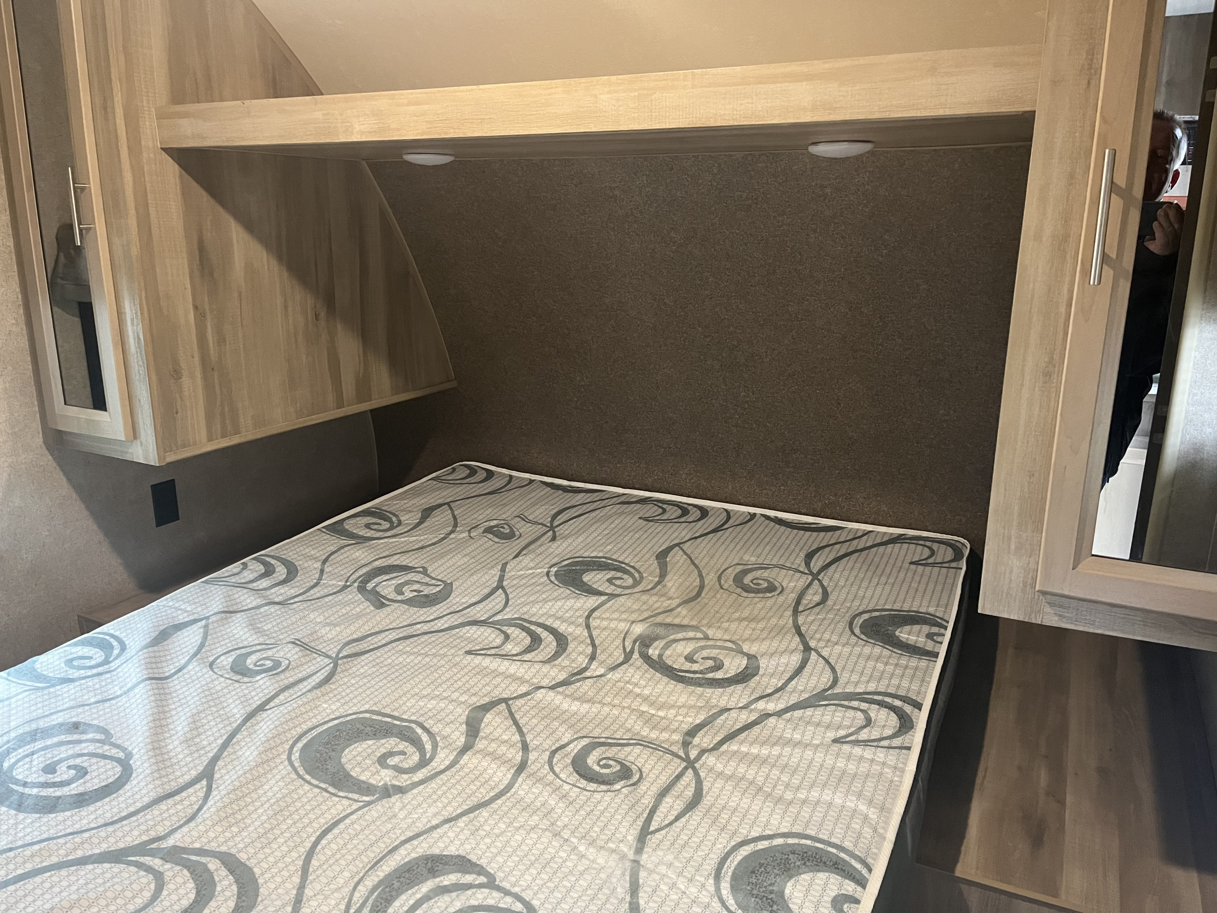 Inside an RV rental: a modern bedroom with a comfortable bed, overhead storage, lighting, and built-in cabinets.. Coachmen Catalina 2020