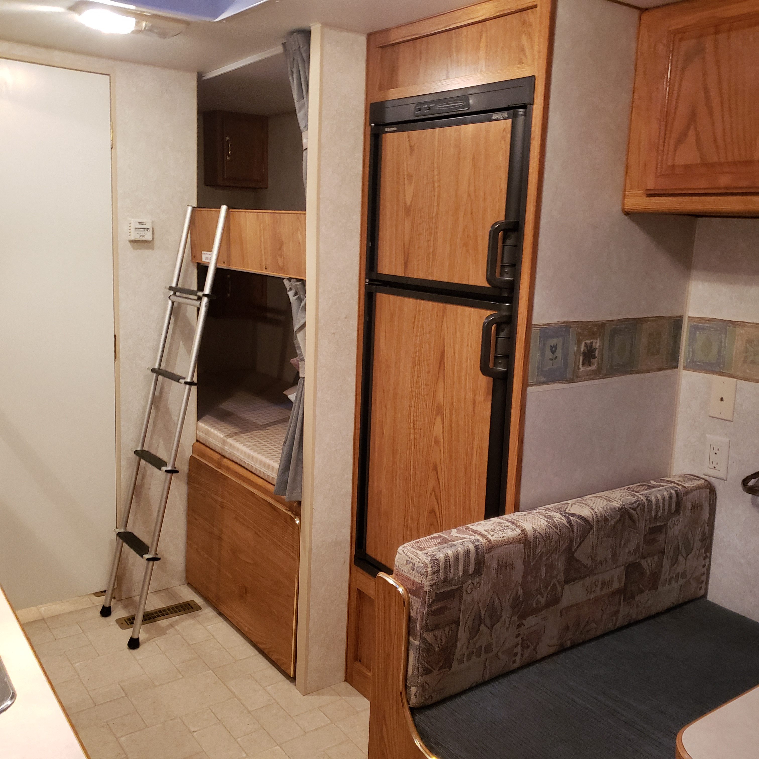 RV rental interior: bunk beds with ladder, large refrigerator, and patterned dinette seating.. Fleetwood Mallard 2004