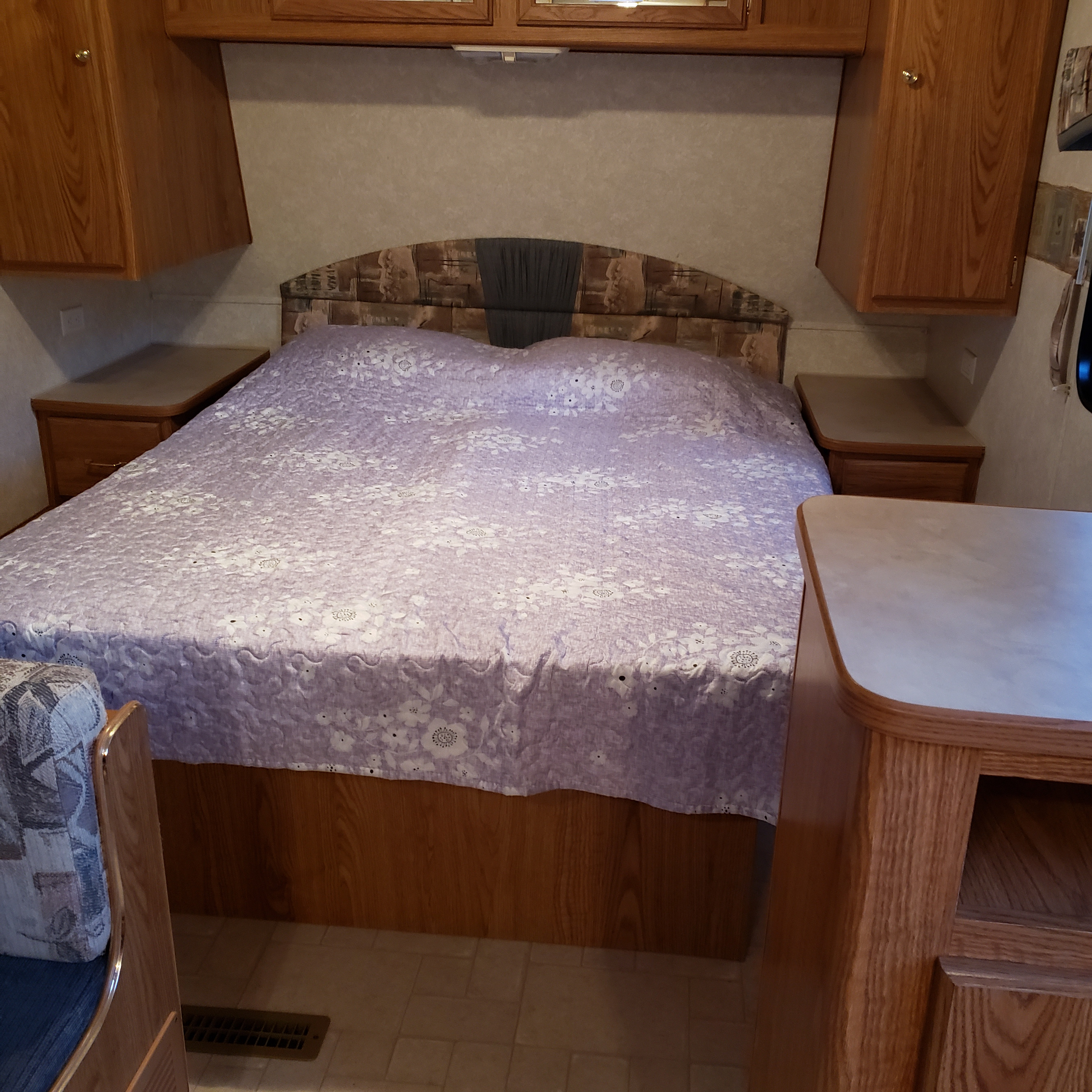 Comfortable RV rental bedroom with a large bed, overhead wood cabinets, and built-in nightstands for travelers.. Fleetwood Mallard 2004