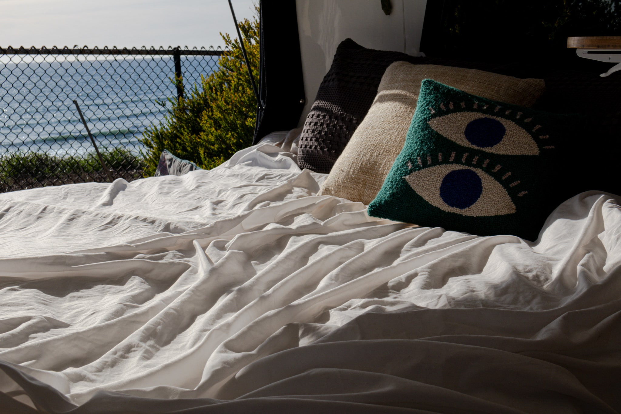 Wake up to ocean views in your cozy RV rental! Rumpled sheets and eye-catching pillows make for a comfy travel bed.. Happier Camper HC1 2024