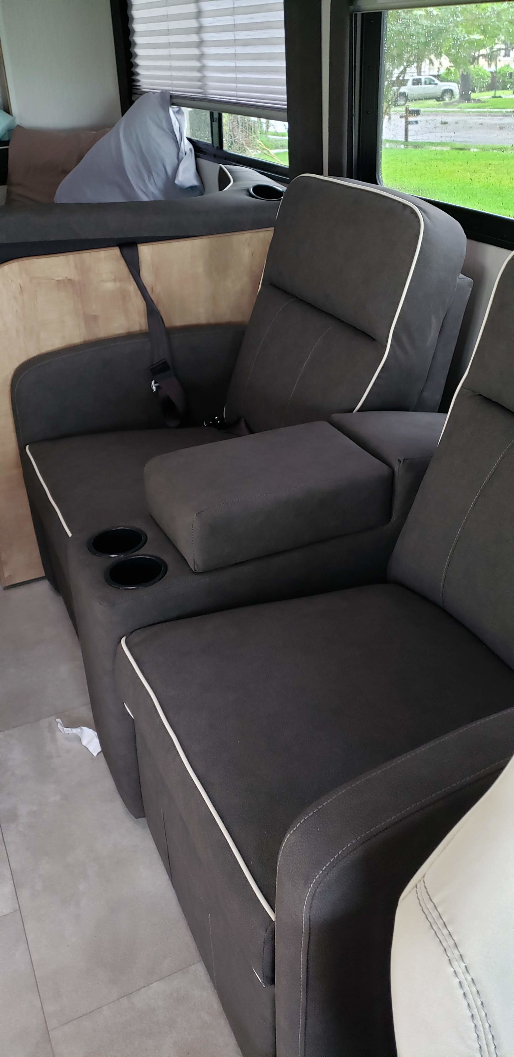 Comfortable RV rental interior with dark gray recliners, armrest console, cup holders, and a side bench with seatbelt.. Forest River Coachmen Leprechaun 2020