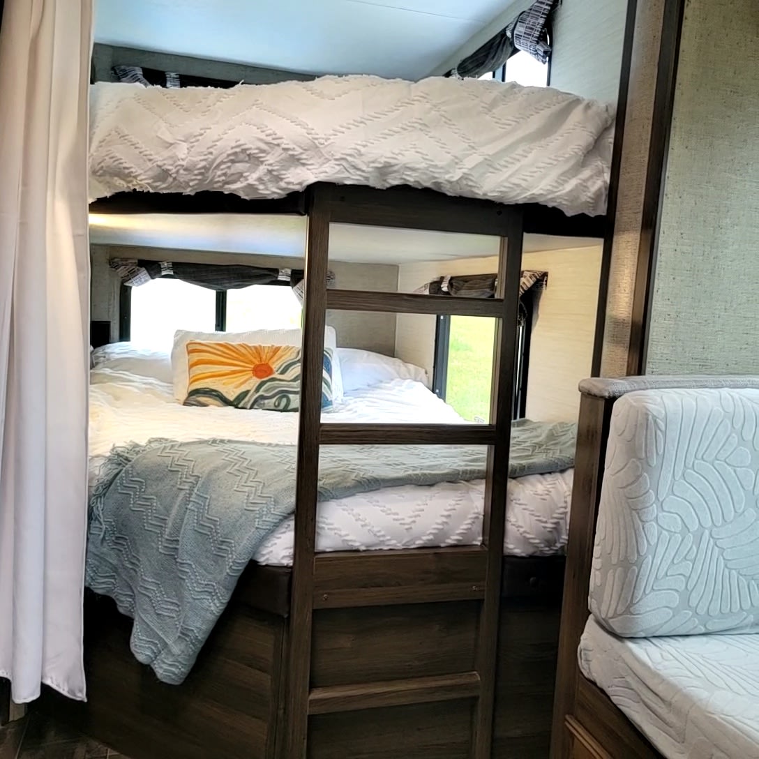 Inside an RV rental: comfortable bunk beds with a ladder. The bottom bunk has white bedding, a blue throw, & decorative pillow.. Keystone RV Bullet Ultra Lite 2018