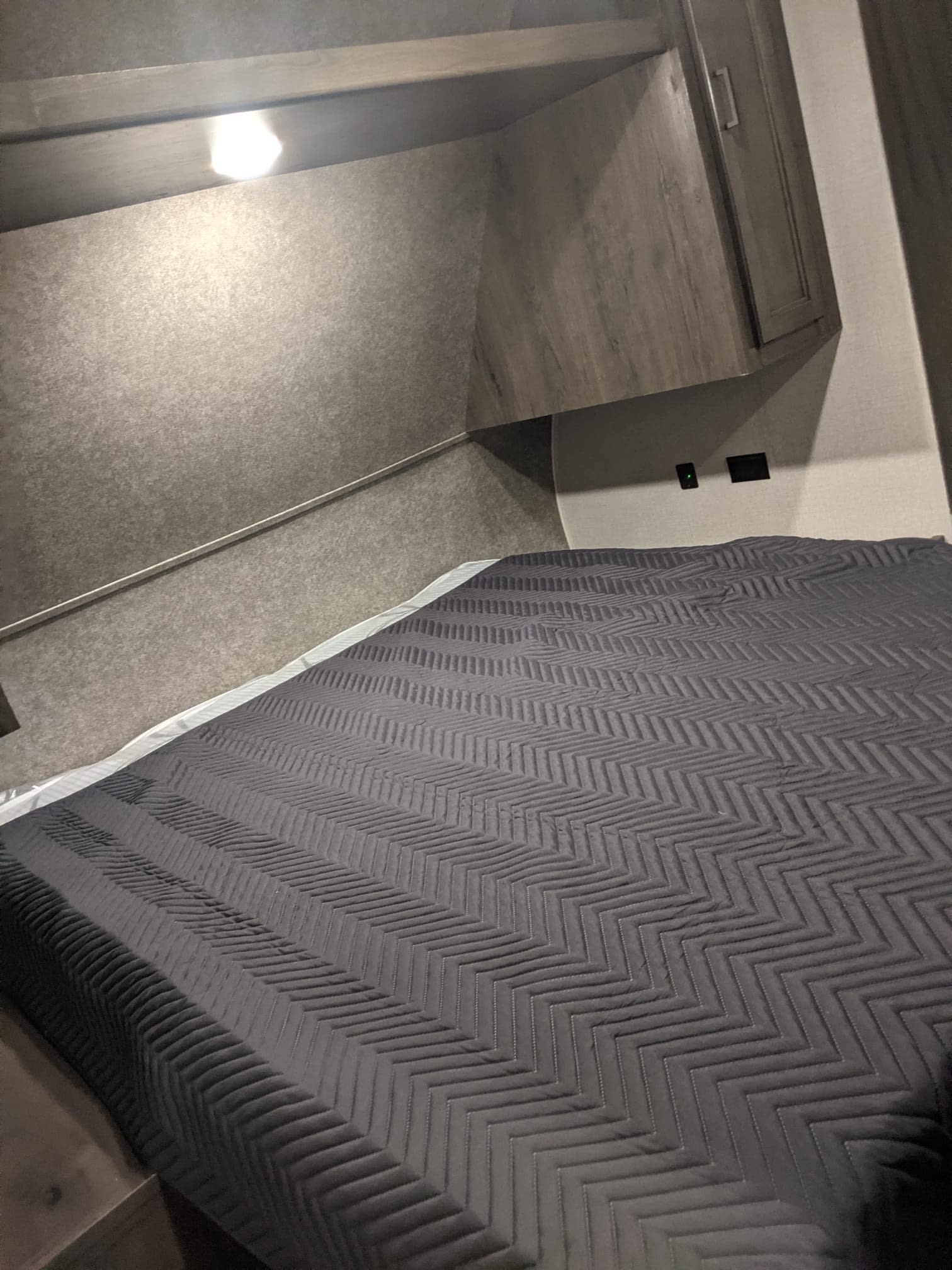 Cozy RV rental bedroom features a comfy bed with a gray chevron quilt, overhead lighting, and compact storage.. Starcraft Autumn Ridge 2021