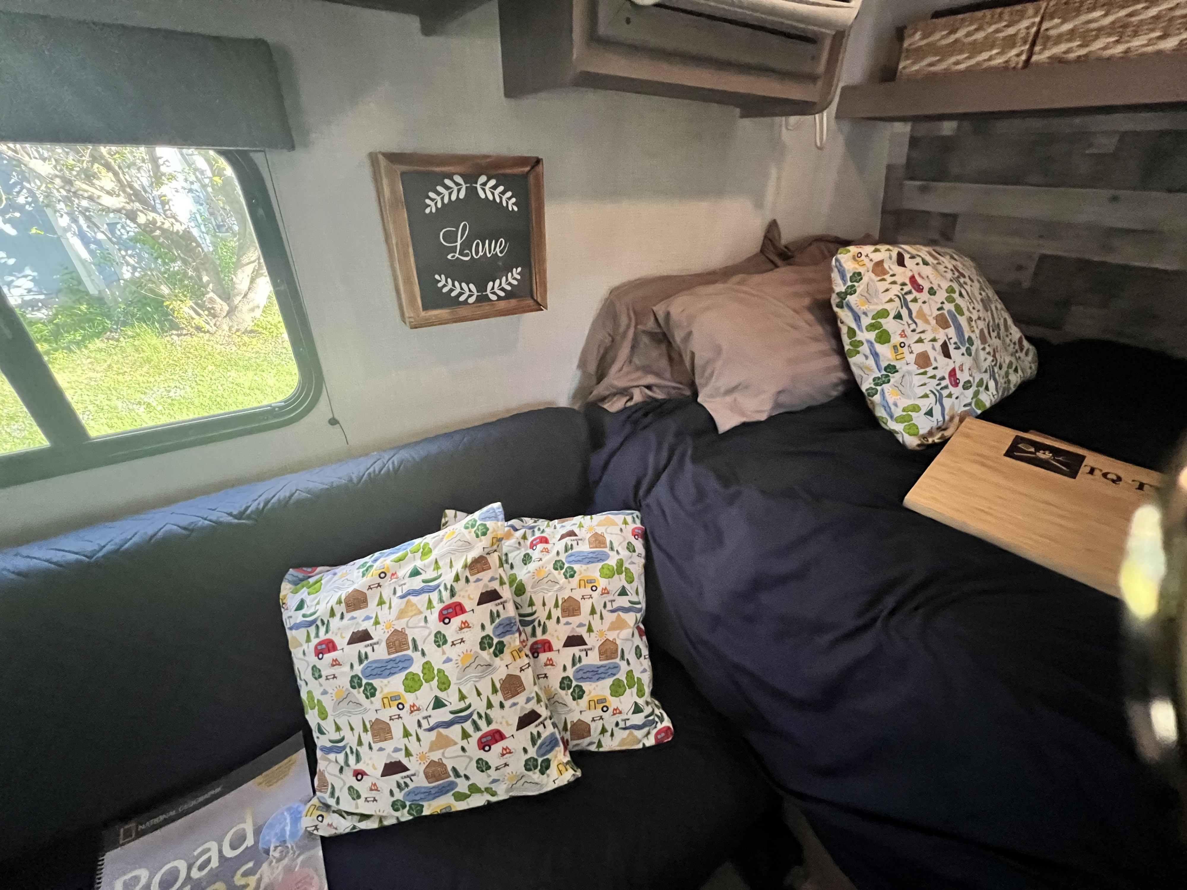 Cozy RV rental interior with a comfy bed, camping-themed pillows, a "Love" sign, and a. Dutchmen Coleman Lantern 2023