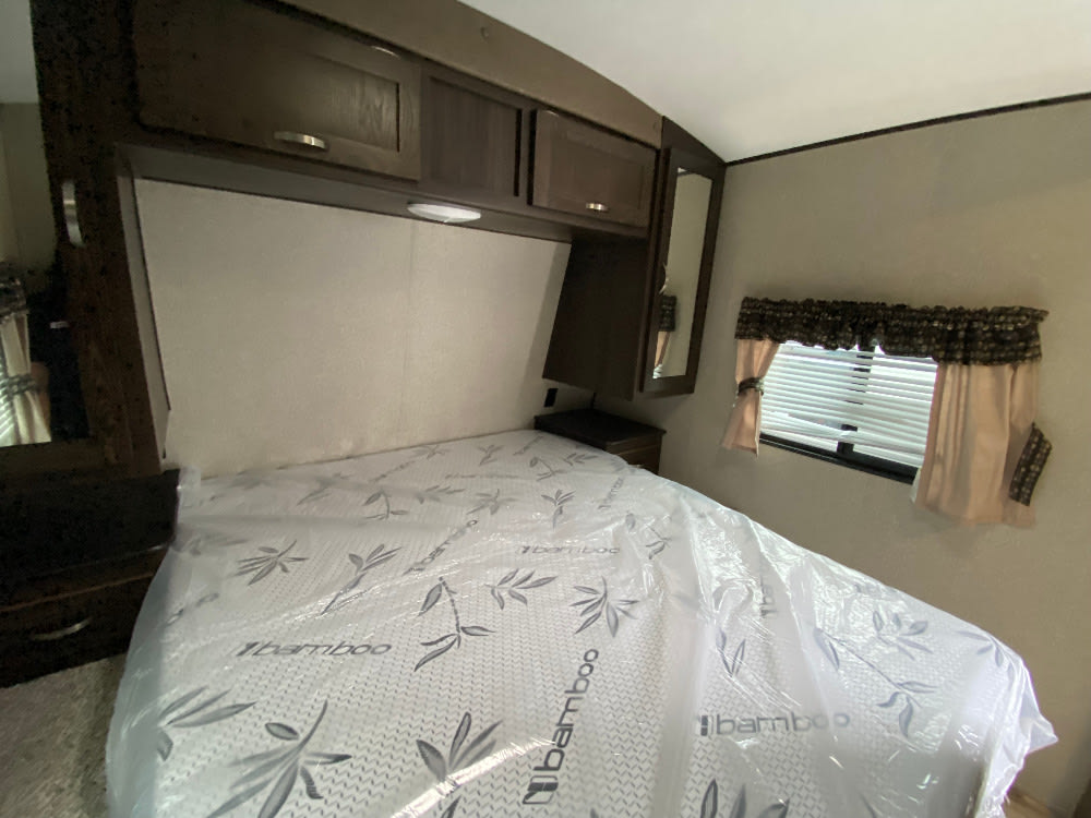 Clean RV rental bedroom featuring a bed with a new bamboo mattress, overhead cabinets, and a window with blinds.. Keystone RV Springdale 2018