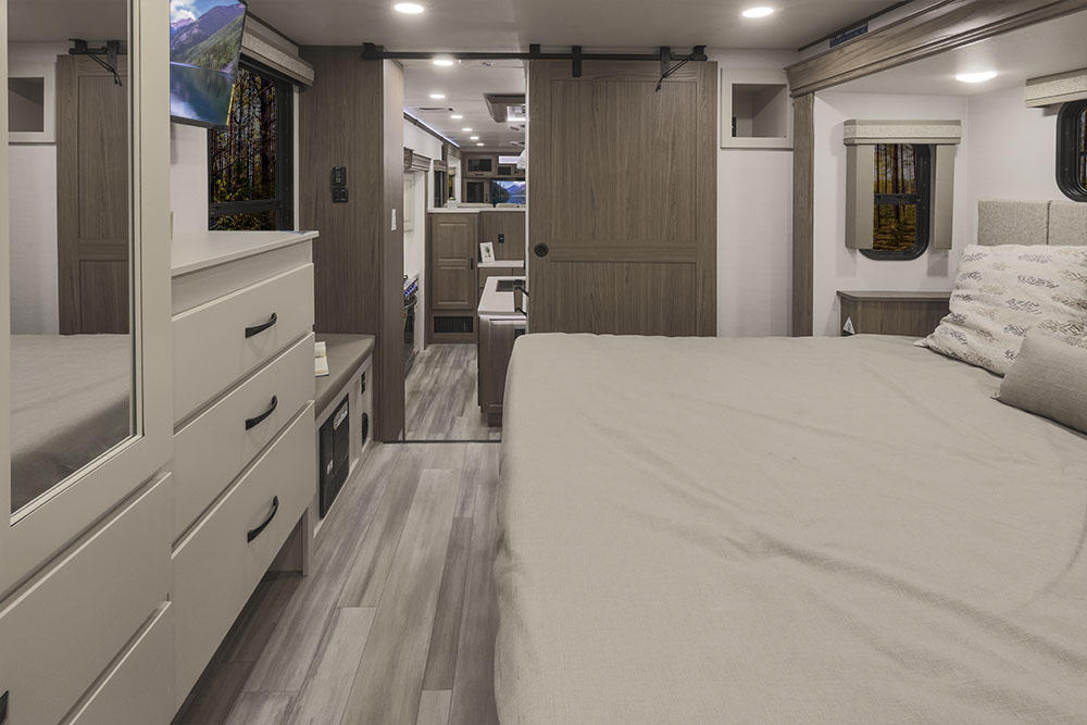 This spacious RV rental bedroom features a comfortable bed, dresser with TV, and a modern sliding barn door, ideal for travel.. Alliance RV Paradigm 2021