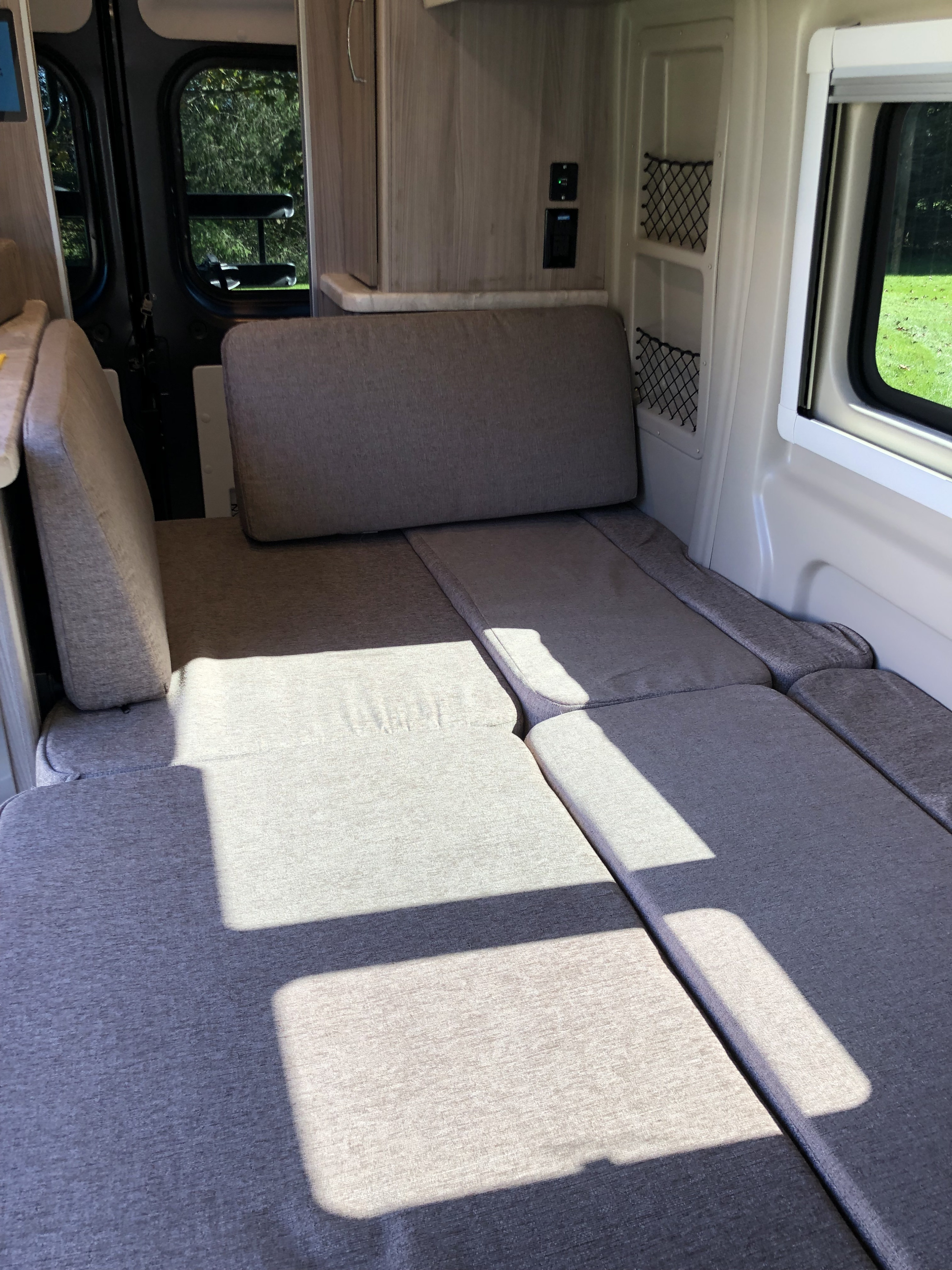 Spacious rv rental interior showing grey convertible seating and bed, bathed in sunlight, perfect for travel comfort.. Thor Other 2022