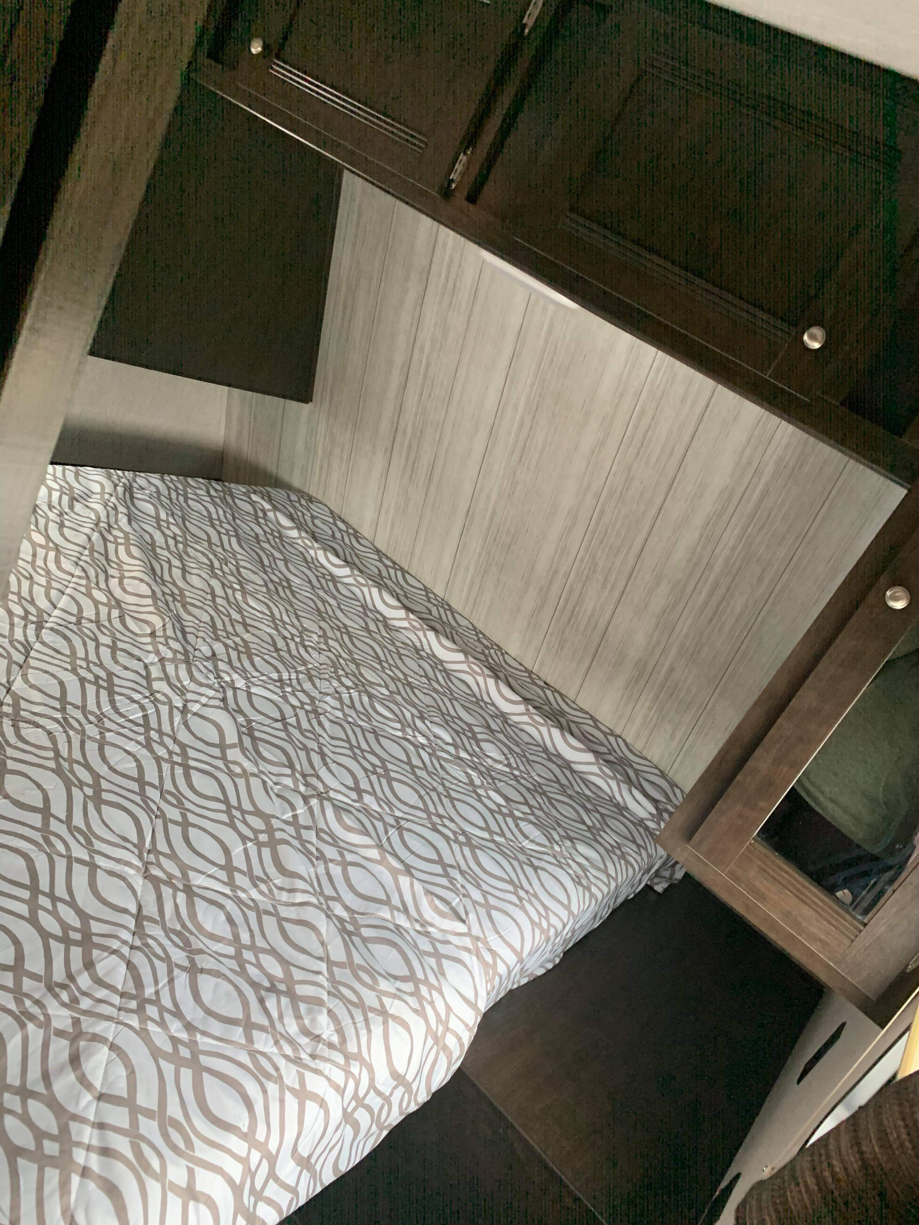 Experience an RV rental bedroom: a compact space with a patterned bed, wood-look walls, and dark built-ins.. Heartland RVs Pioneer 2019