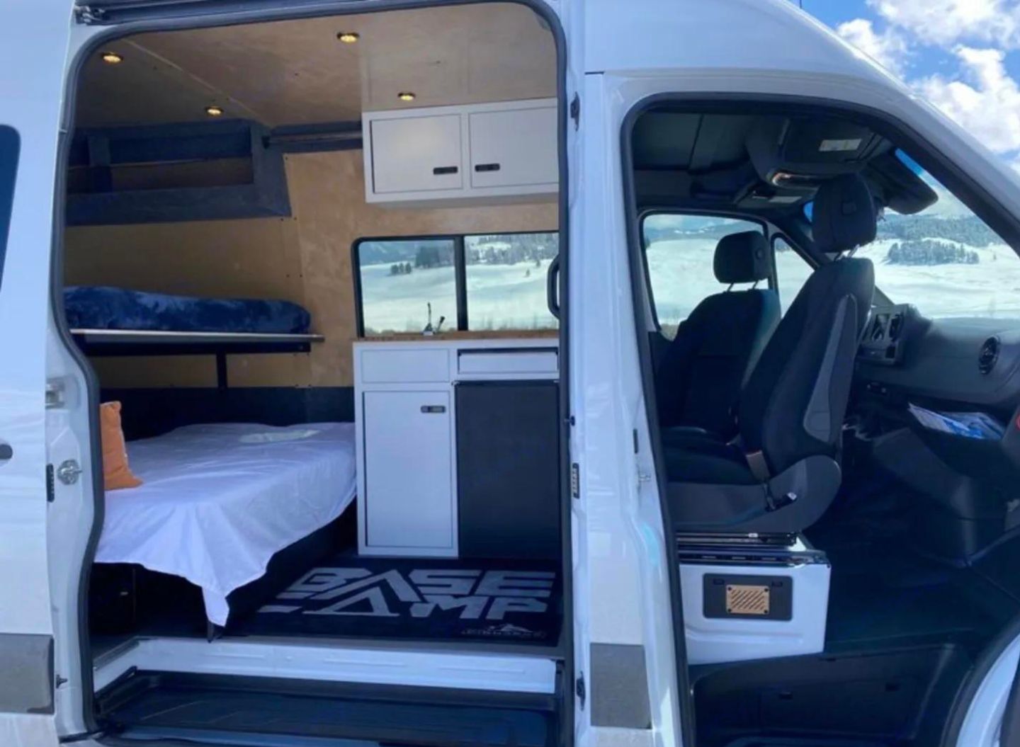 Inside this spacious RV rental camper van: multiple beds, a mini-kitchen, & driver's area. Snowy landscape visible outside.. Vanworks Base Camp 2021