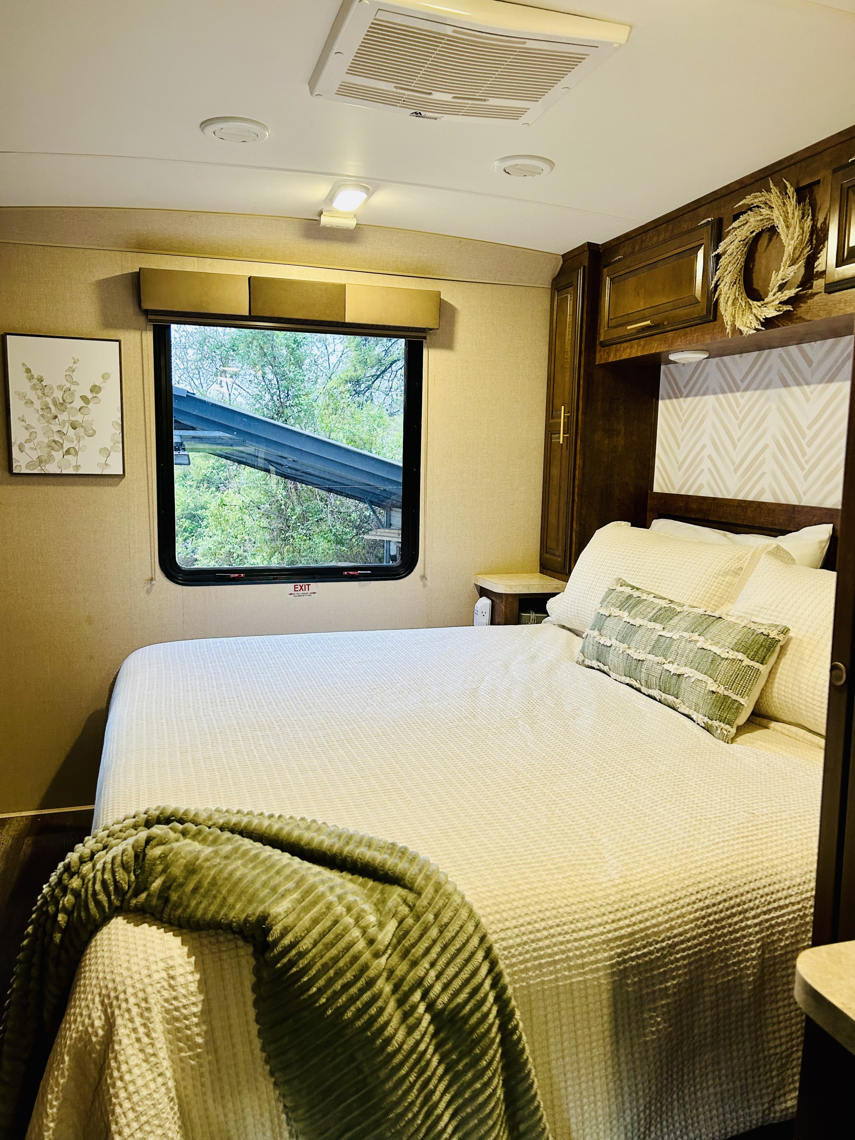 Cozy RV rental bedroom featuring white bedding, a green throw, wood cabinets, and a window view of lush trees. Ideal for travel.. FR3 FR3 Motorhome 2016