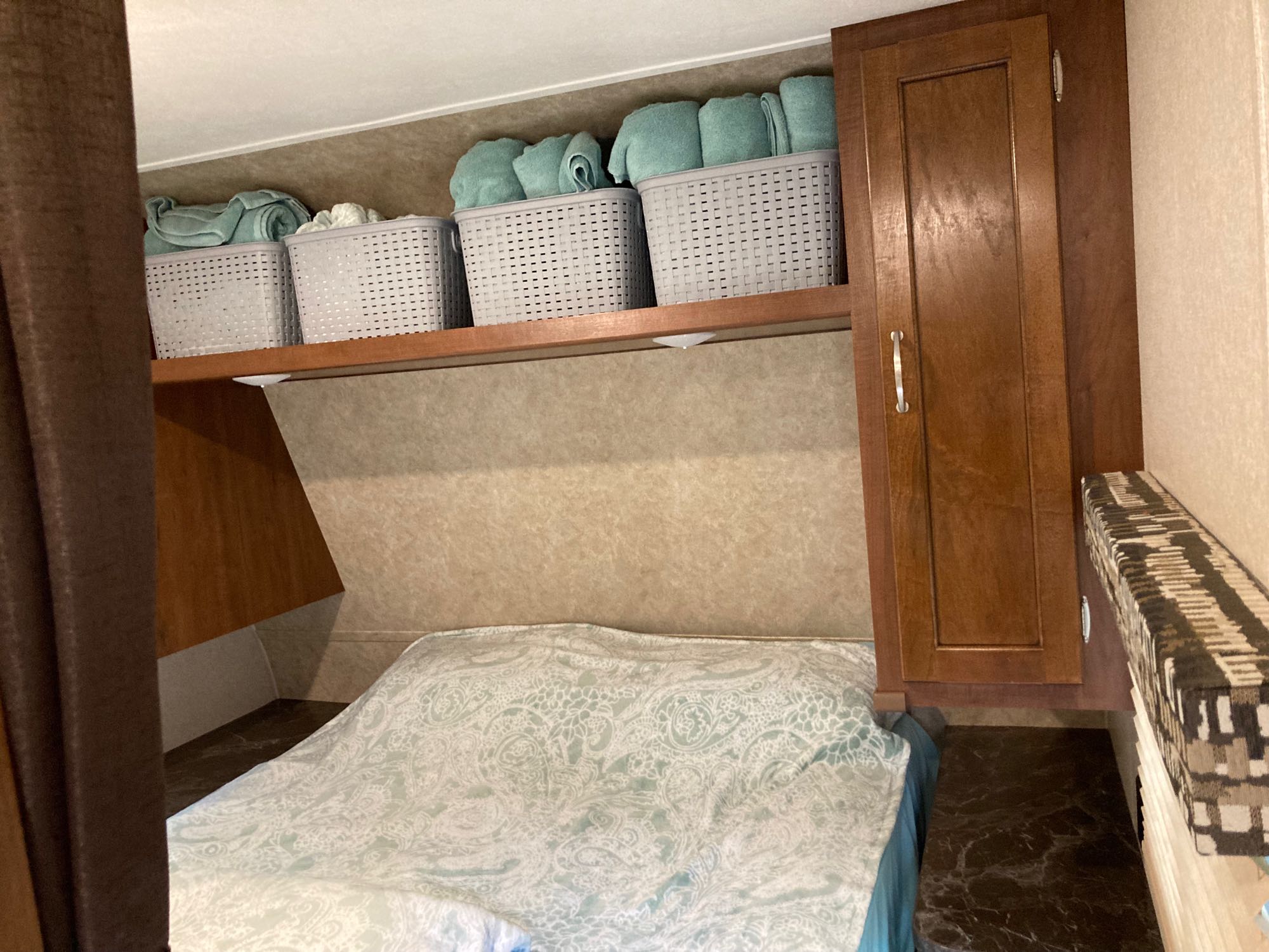 Cozy RV rental bedroom with a neatly made bed, organized overhead storage baskets filled with towels, and a wooden cabinet.. Jayco Jay Flight SLX 2017