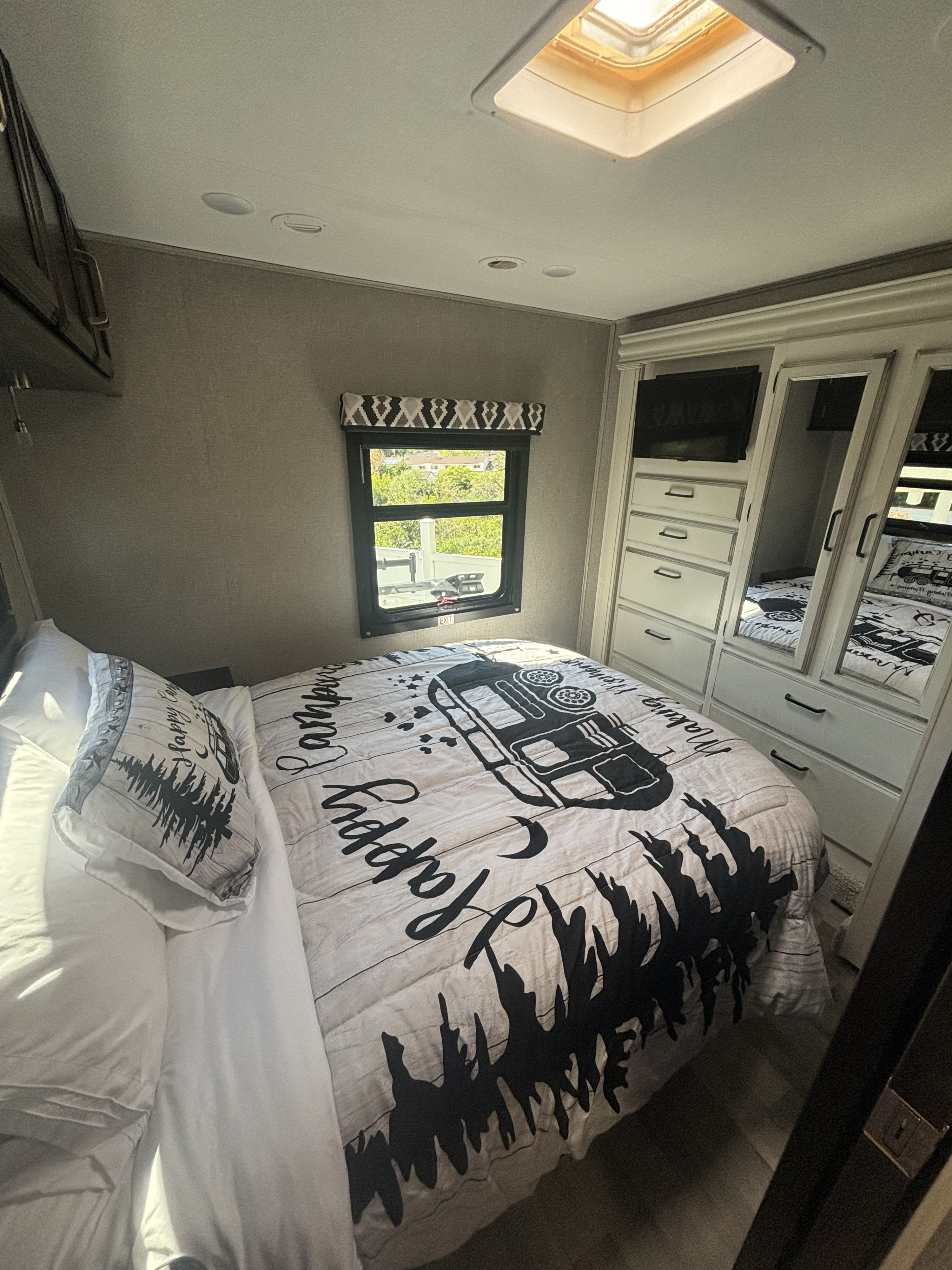 Spacious RV rental bedroom with 'Happy Camping' bedding, window, mirrored closets, and ceiling skylight.. Entegra Coach Odyssey 2021
