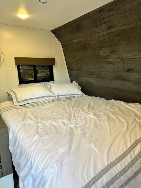 Comfortable RV rental bedroom featuring a neatly made bed with white and gray bedding, a window, and wood-look interior walls.. Keystone RV Hideout 2022