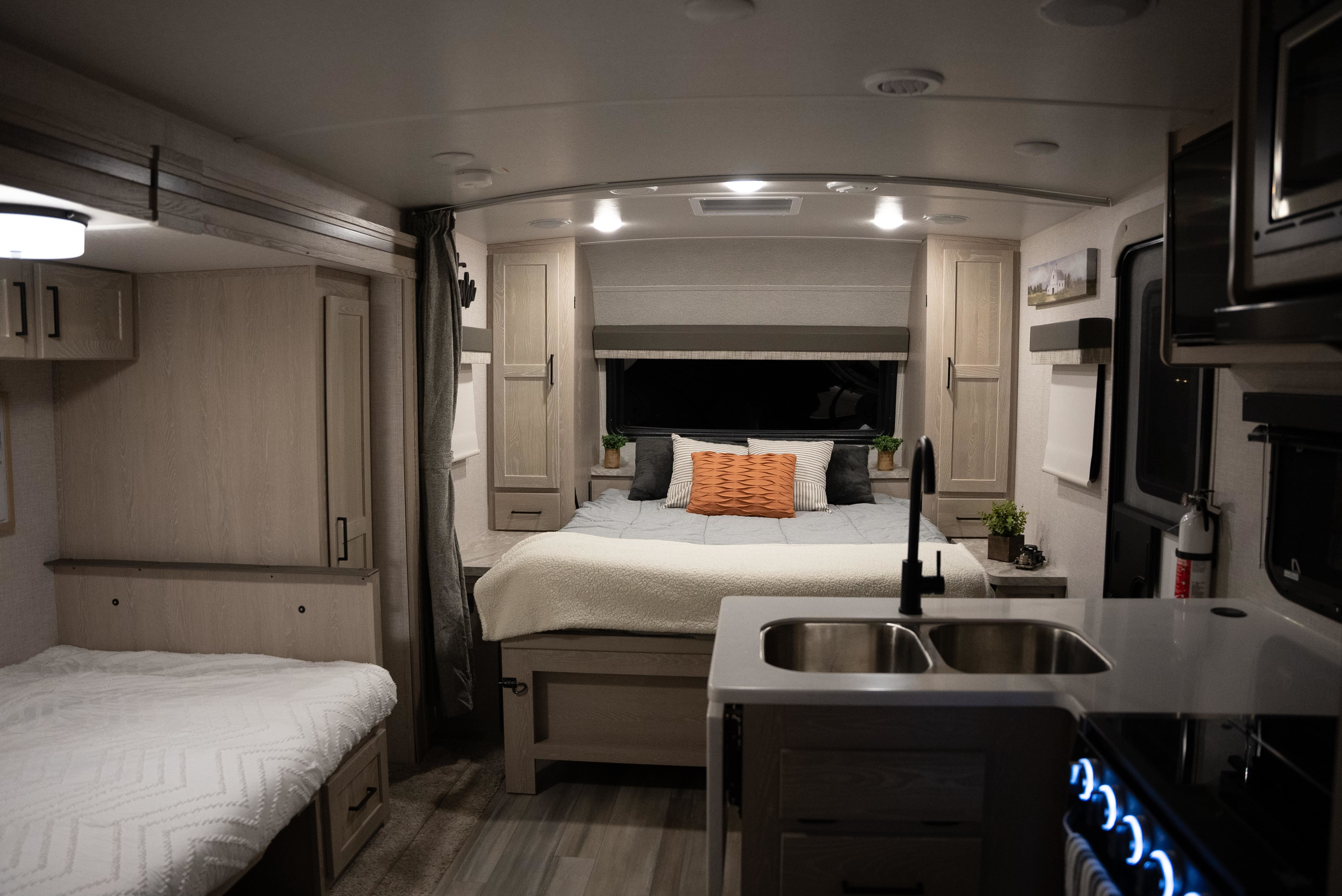 Inside a modern RV rental: a cozy bedroom with light wood cabinetry and a functional kitchen with a sink and lighted stovetop.. Forest River Flagstaff Micro Lite 2022