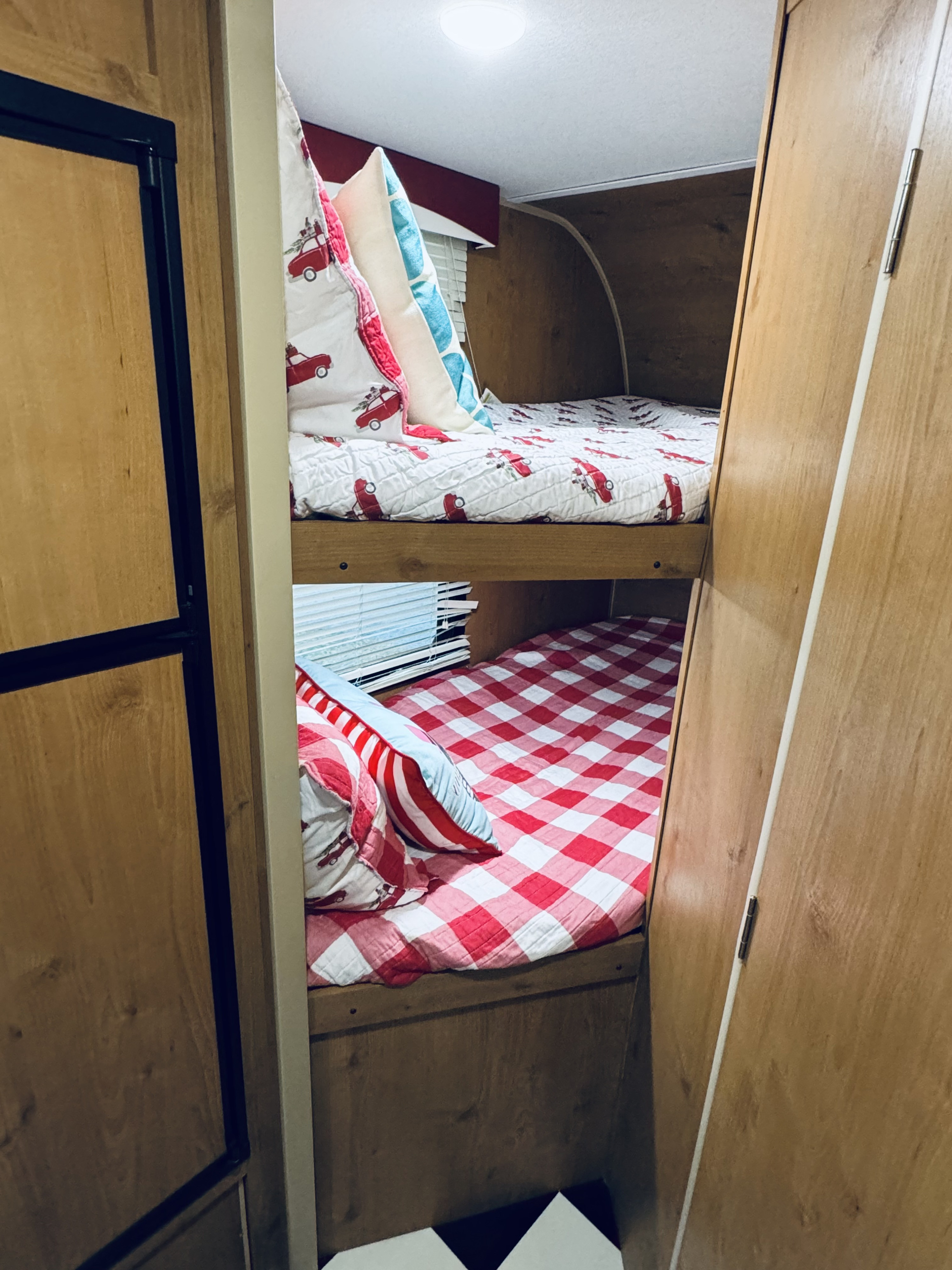 Cozy RV rental bunk beds, with one featuring red trucks and the other red/white checks, offer comfortable sleeping.. Riverside RV Retro 2021