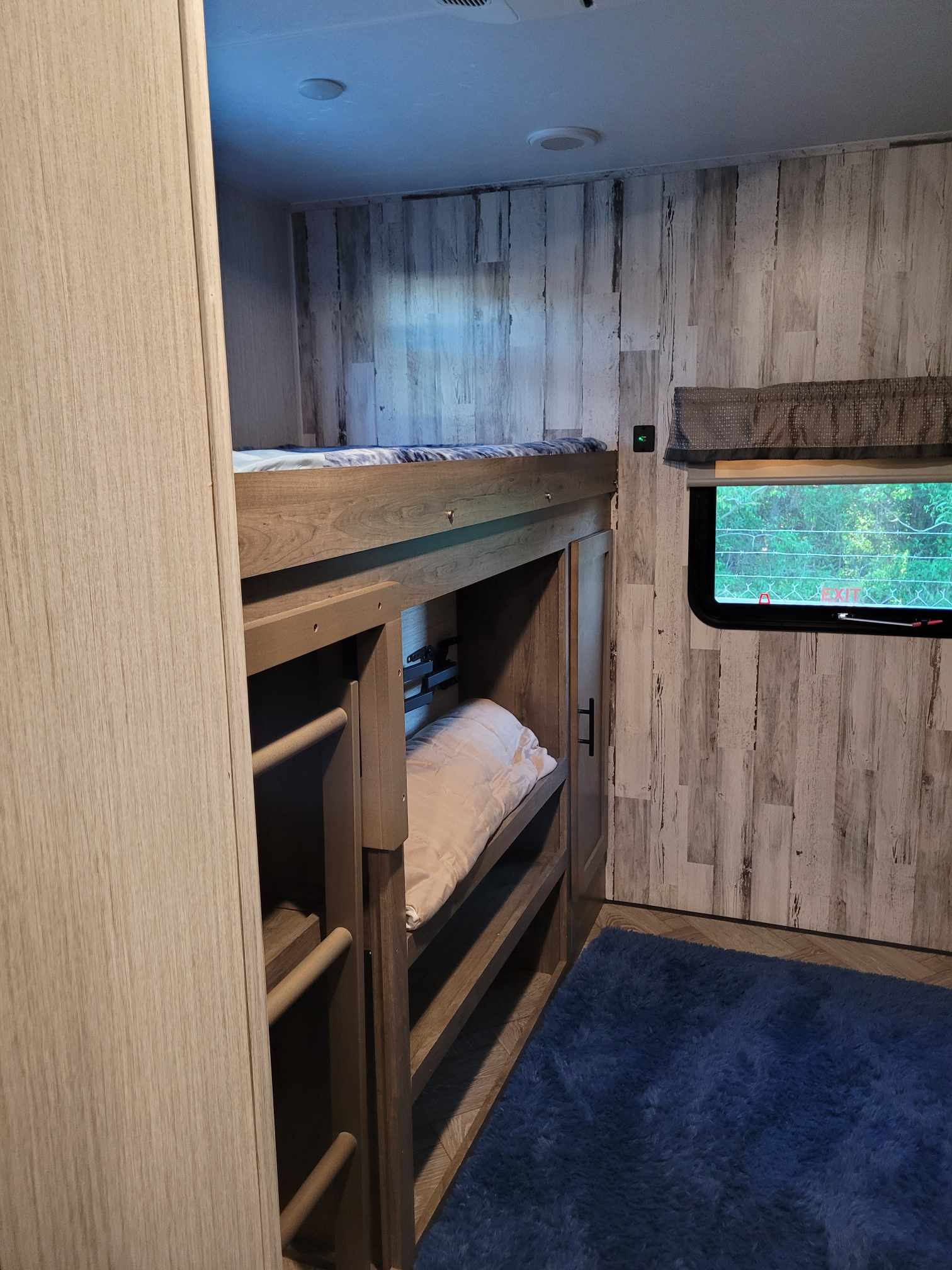 Cozy RV rental bedroom with bunk beds, wood-look walls, a window overlooking nature, and a soft blue rug.. Forest River Palomino Puma 2021