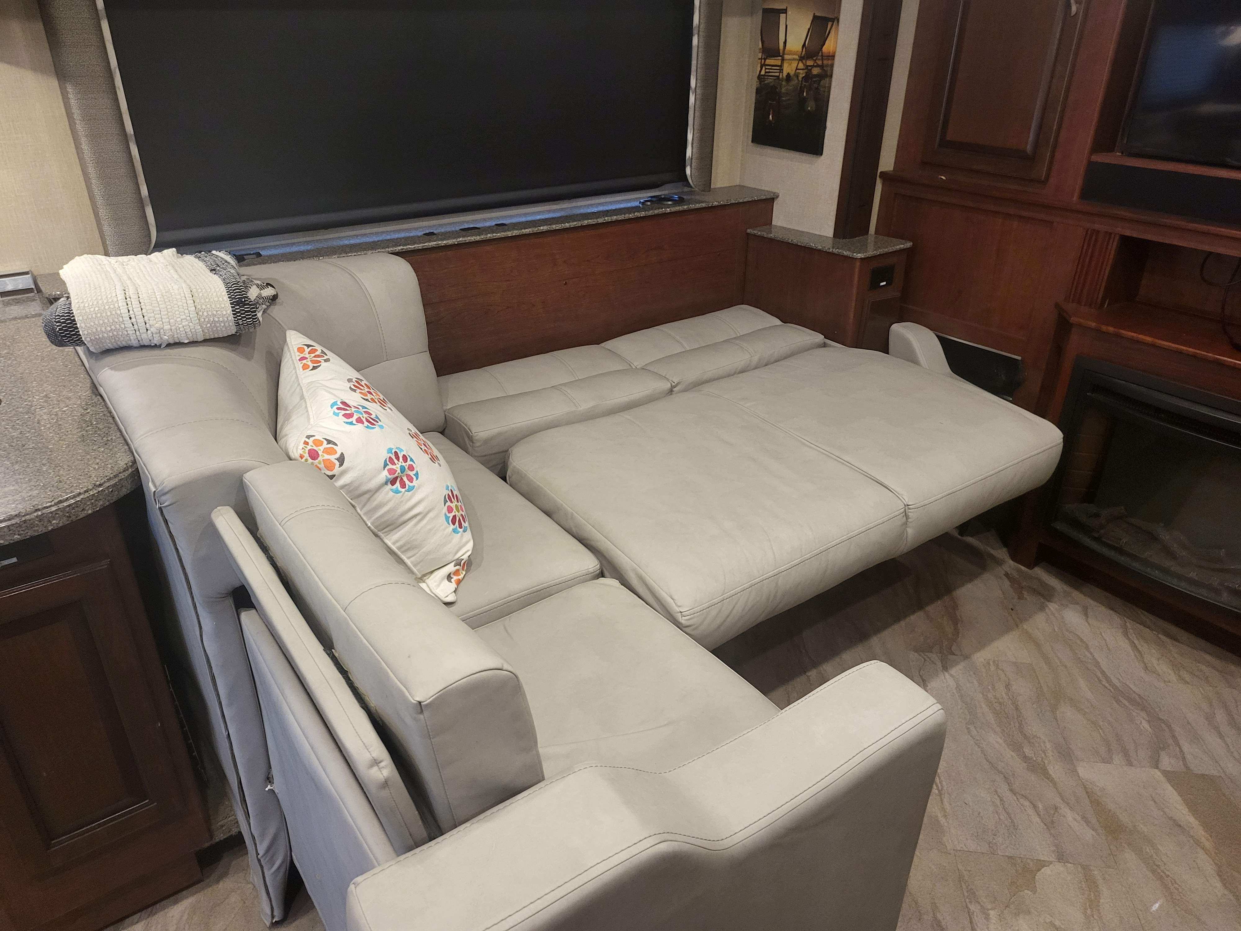 A light gray L-shaped sectional sofa, partially extended into a bed, in an RV rental living area.. Fleetwood Bounder 2017