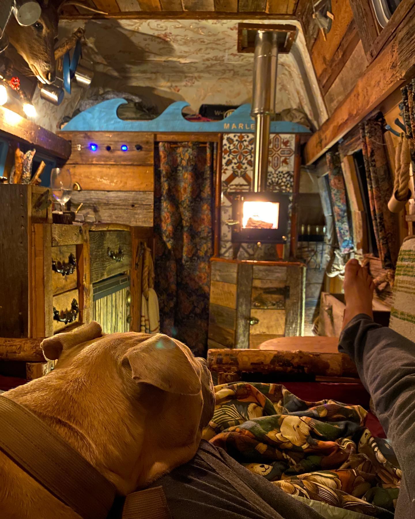 Cozy RV rental: A dog and person unwind by the wood stove in a charming, custom-built interior, perfect for relaxation.. Ford Econoline Club Wagon 1985