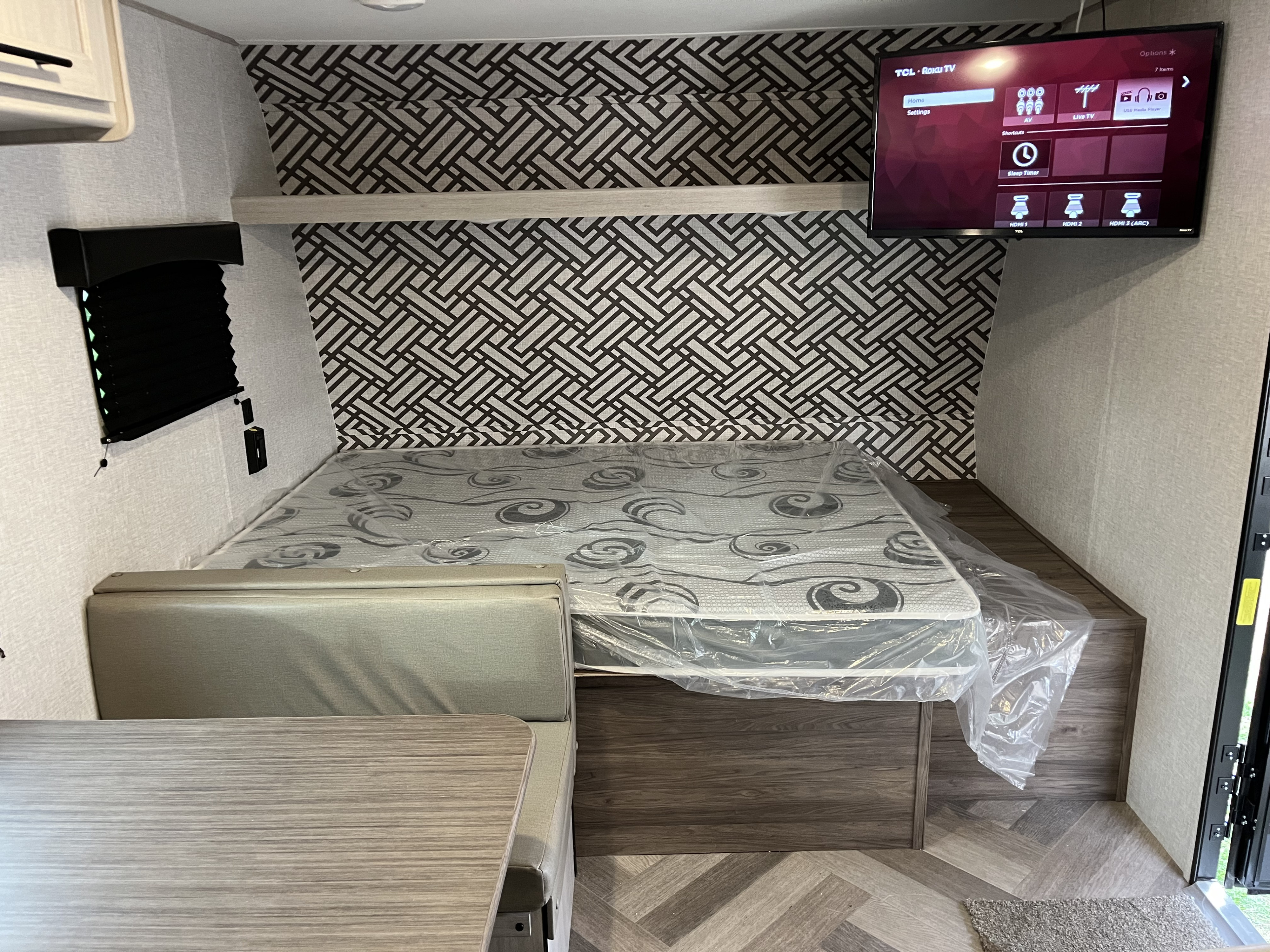 Modern RV rental interior with a geometric wall, new mattress, dinette, and a TCL Roku TV for entertainment.. Crossroads RV Zinger Lite 2024