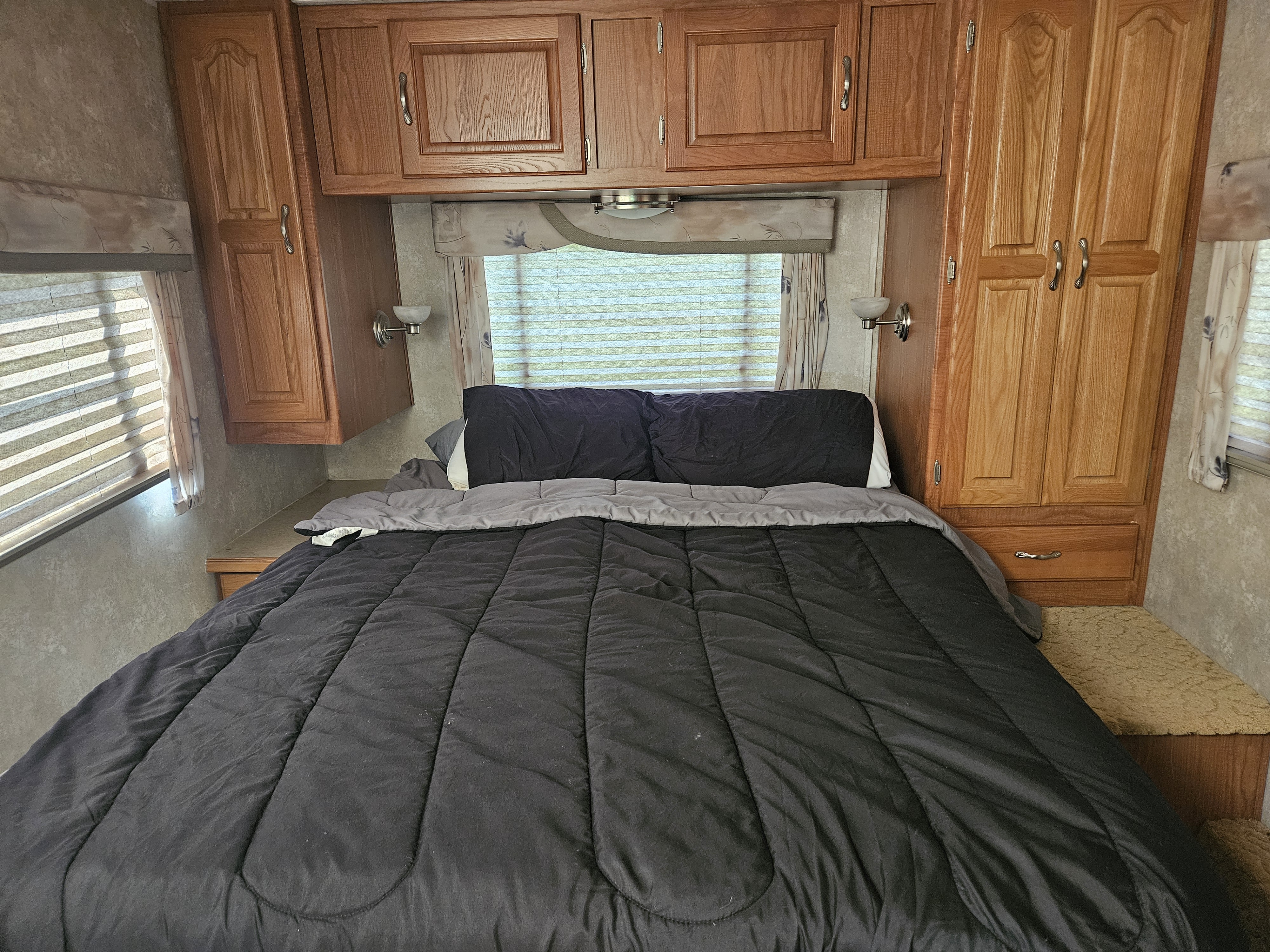 Cozy RV rental bedroom with a full bed, wood cabinets, and window blinds, providing comfort in a compact space.. Coachmen Leprechaun 2003
