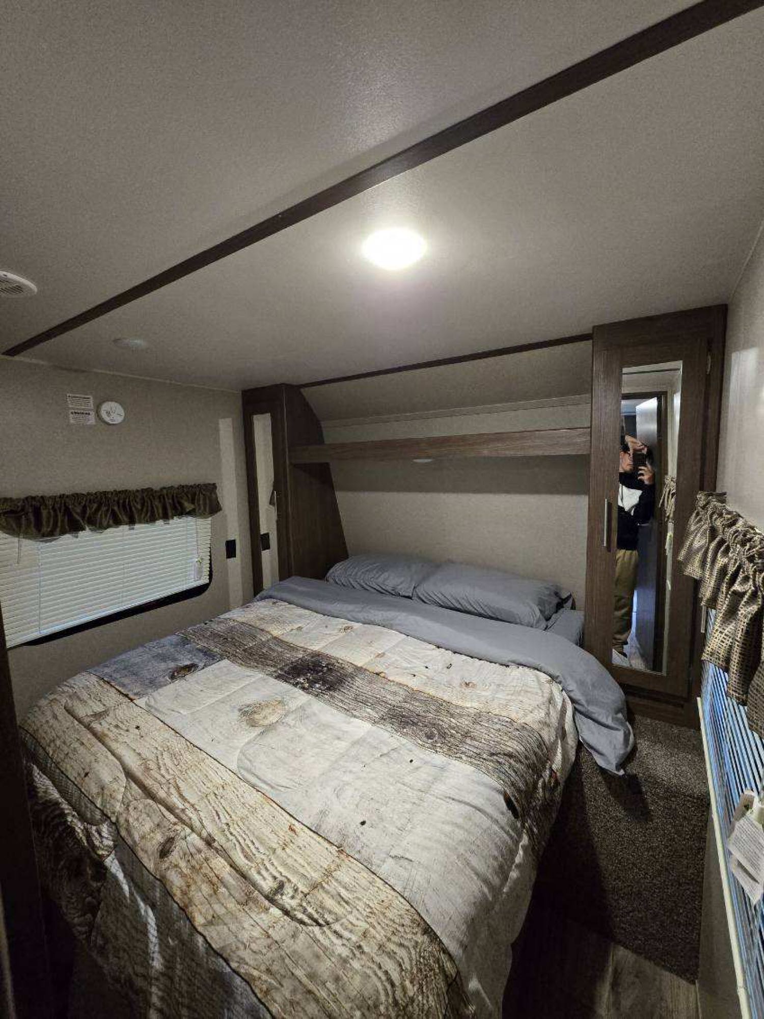 RV rental bedroom interior: Features a cozy bed with unique wood-patterned comforter, window, and mirrored closet.. Keystone RV Hideout Luxury 2019