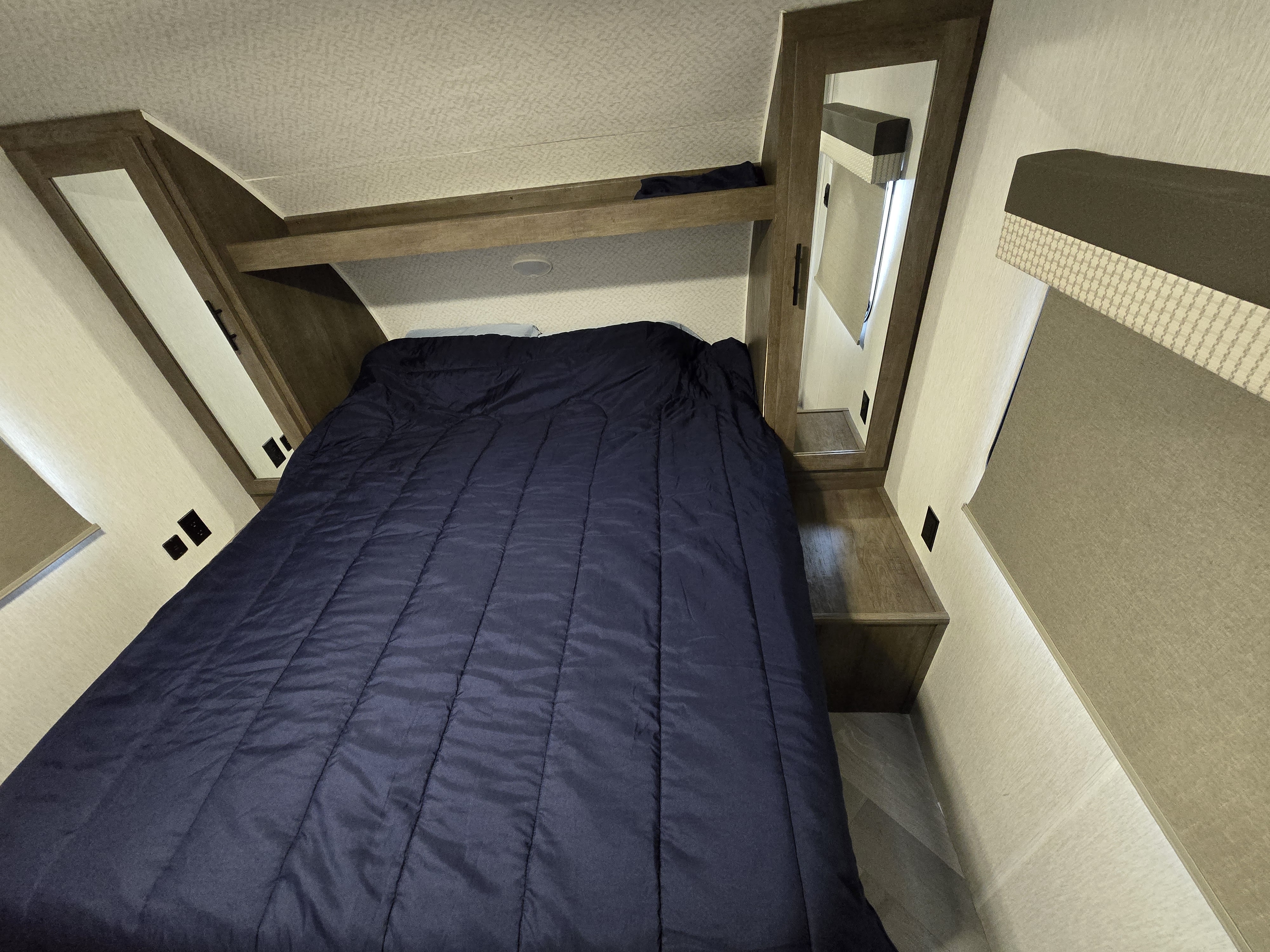 Cozy RV rental bedroom with a dark blue bed, built-in wooden storage cabinets, mirrors, and an overhead shelf.. Forest River Wildwood X-Lite 2022