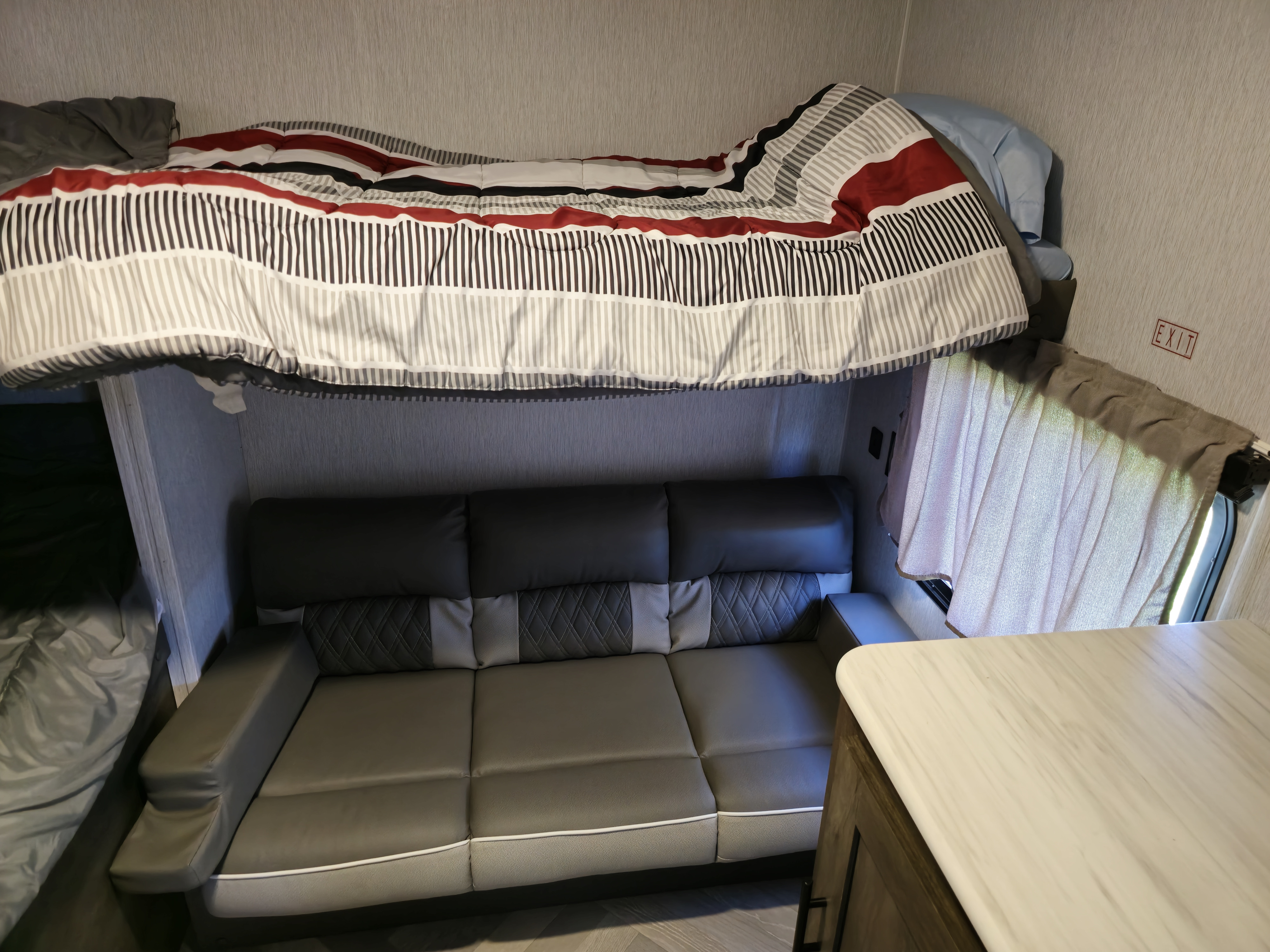 RV rental interior shows a bunk bed with striped bedding over a gray sofa. Compact, functional living space.. Forest River Wildwood X-Lite 2022
